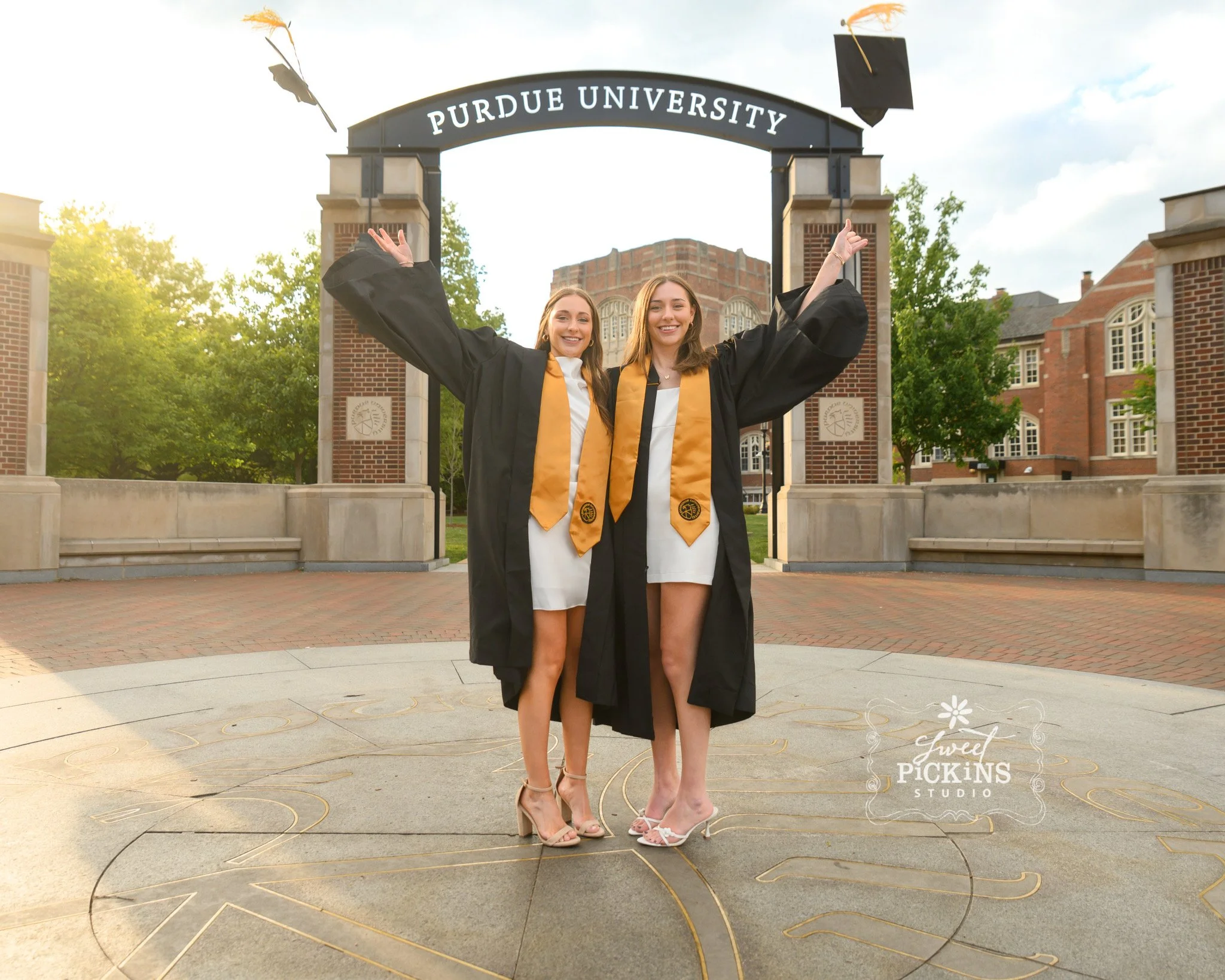 Purdue University Graduation Photography for Twins Class of 2026 Sisters pose at Memorial Union arch in West Lafayette, Indiana by Sweet Pickins Studio senior photographer Amanda Wilson ©