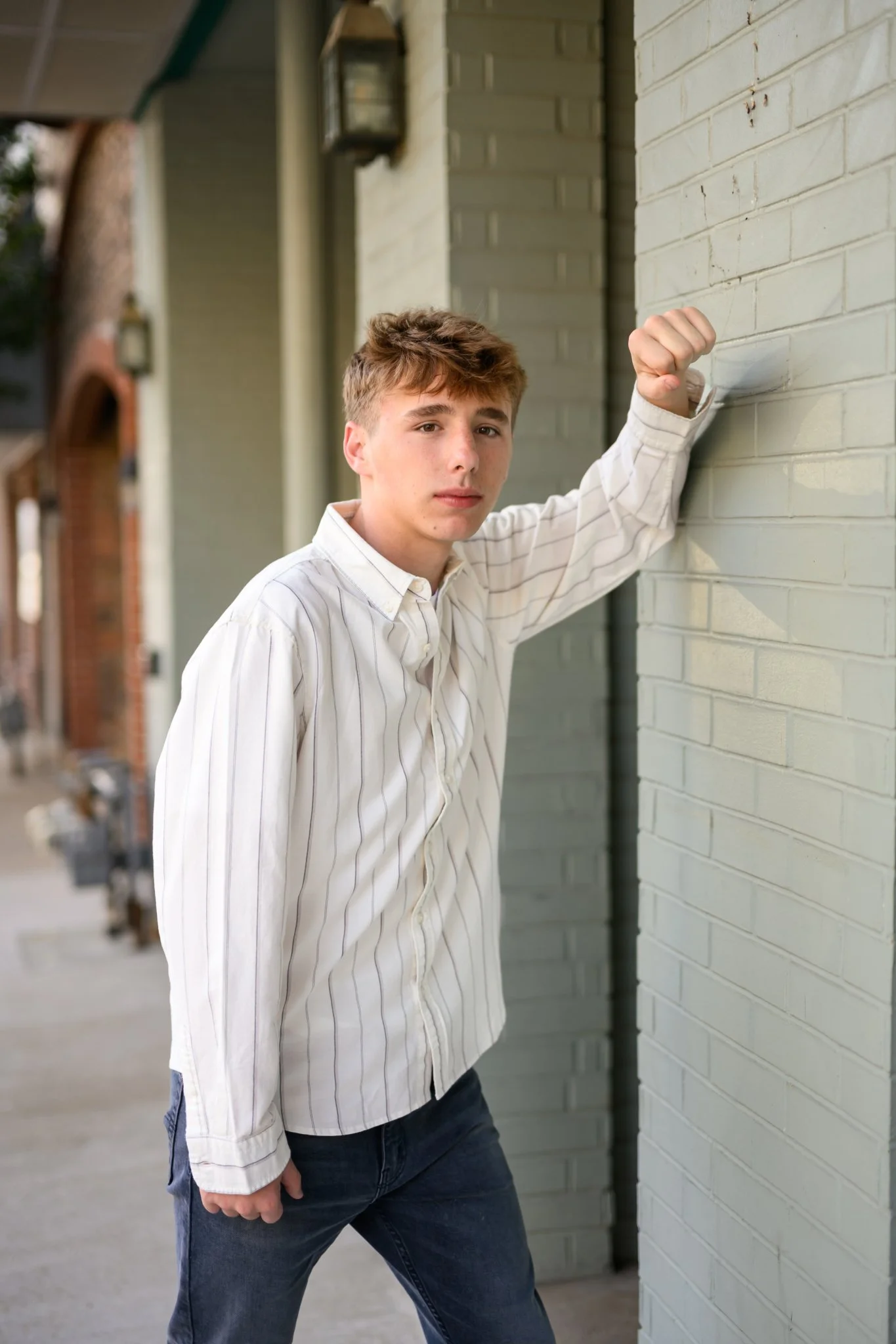 Huntington, Indiana Senior Guy Portraits for Huntington North Class of 2027 Senior boy BOSTAN leaning on wall in denim jean button down shirt in urban downtown by Sweet Pickins Studio senior photographer Amanda Wilson ©