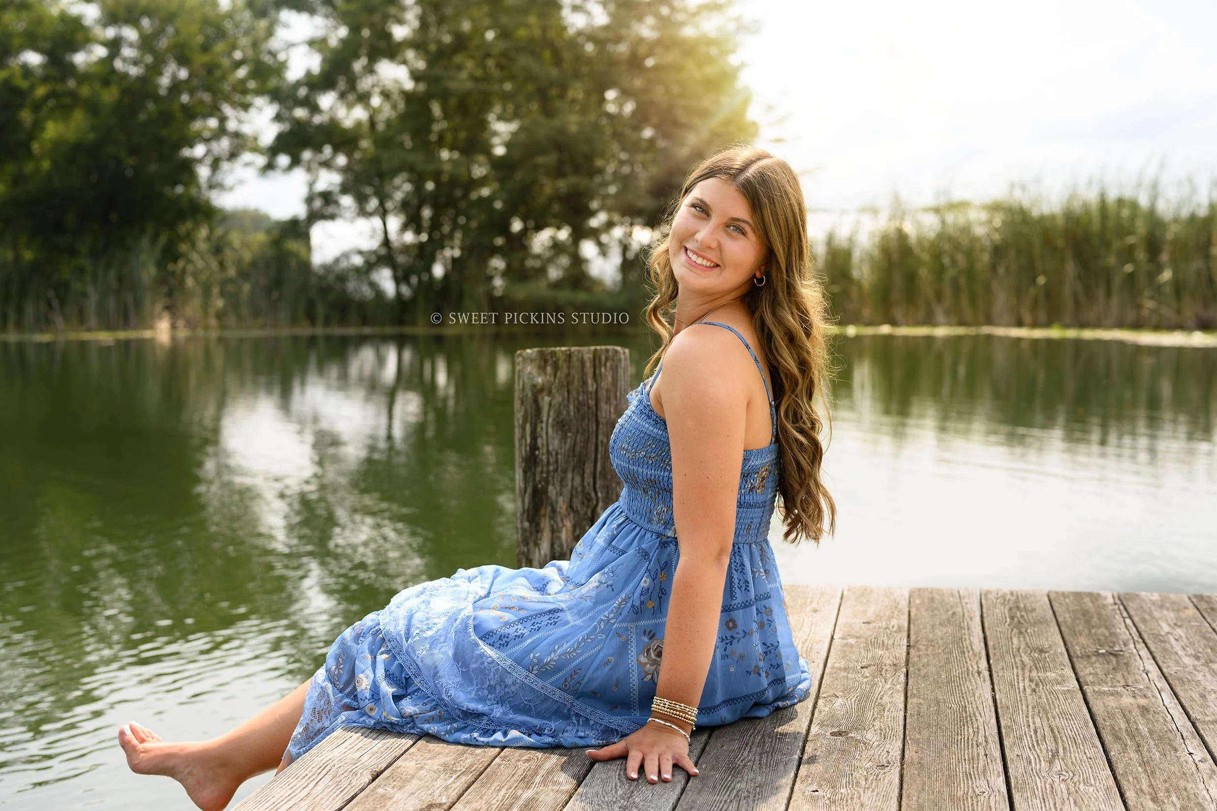 Zionsville, Indiana Senior Photography at Traders Point Creamery with class of 2027 senior girl posing in blue sun dress on wood pier at pond by Sweet Pickins Studio senior photographer Amanda Wilson ©