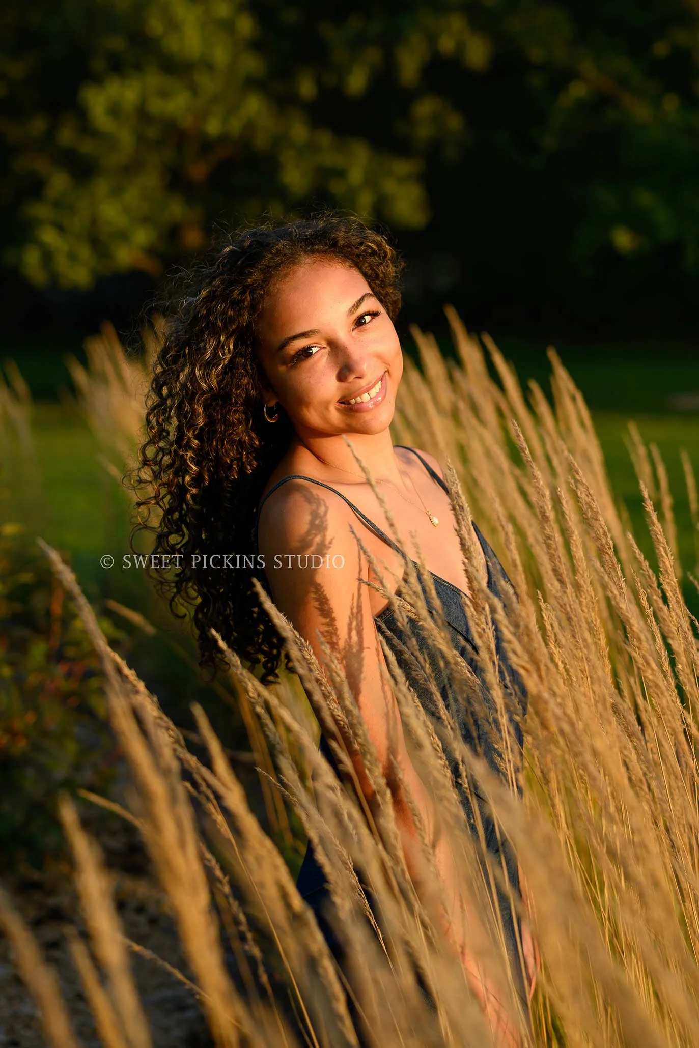 Madeline | Golden Hour Senior Photography for Class of 2027 senior girl with curly hair wearing denim jean dress in golden grass by Peru Indiana Senior  photographer Amanda Wilson of Sweet Pickins Studio ©
