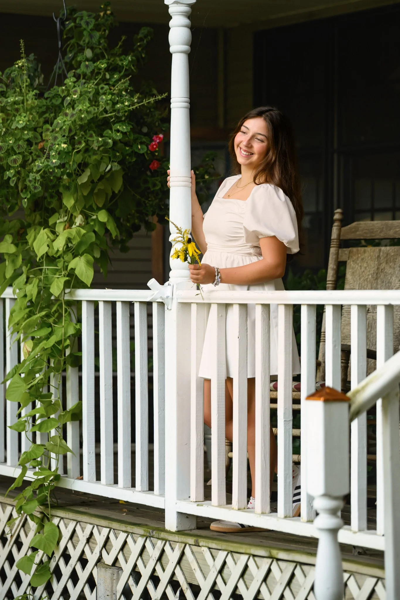 Maisie | Lakeville, Indiana Senior Portrait Photography on Porch for Madison East High School class of 2027 senior girl posing in white dress holding yellow flowers by Peru Indiana senior photographer Amanda Wilson © Sweet Pickins Studio
