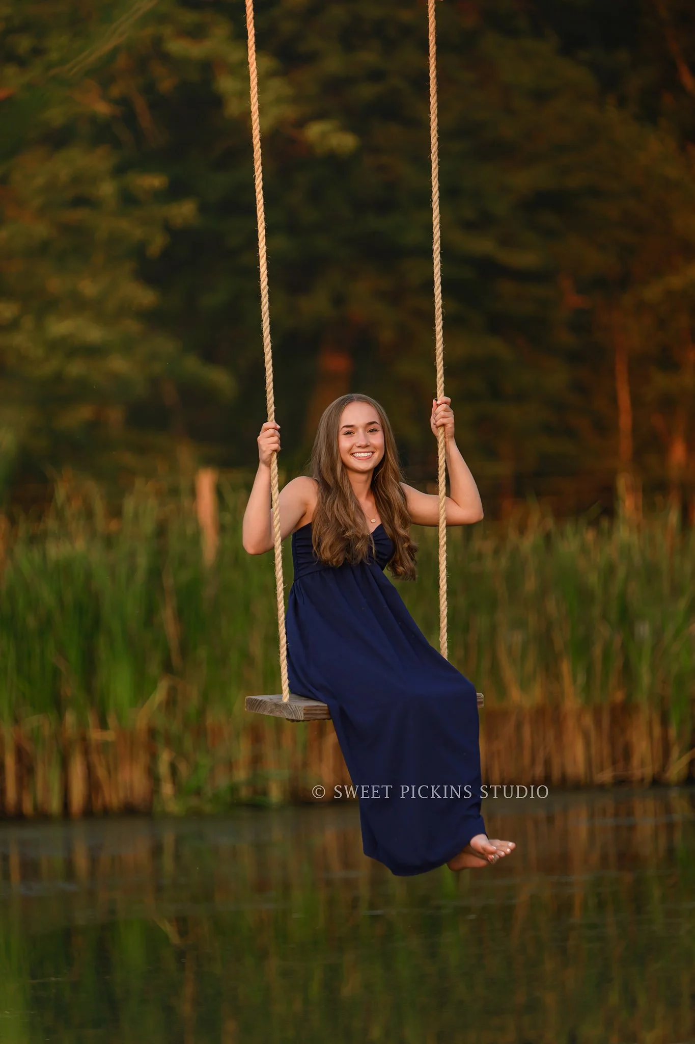 Natalie’s Lowell, Indiana Senior Photography posing on rope swing in blue dress over pond at sunset on farm by Sweet Pickins Studio senior photographer Amanda Wilson ©
