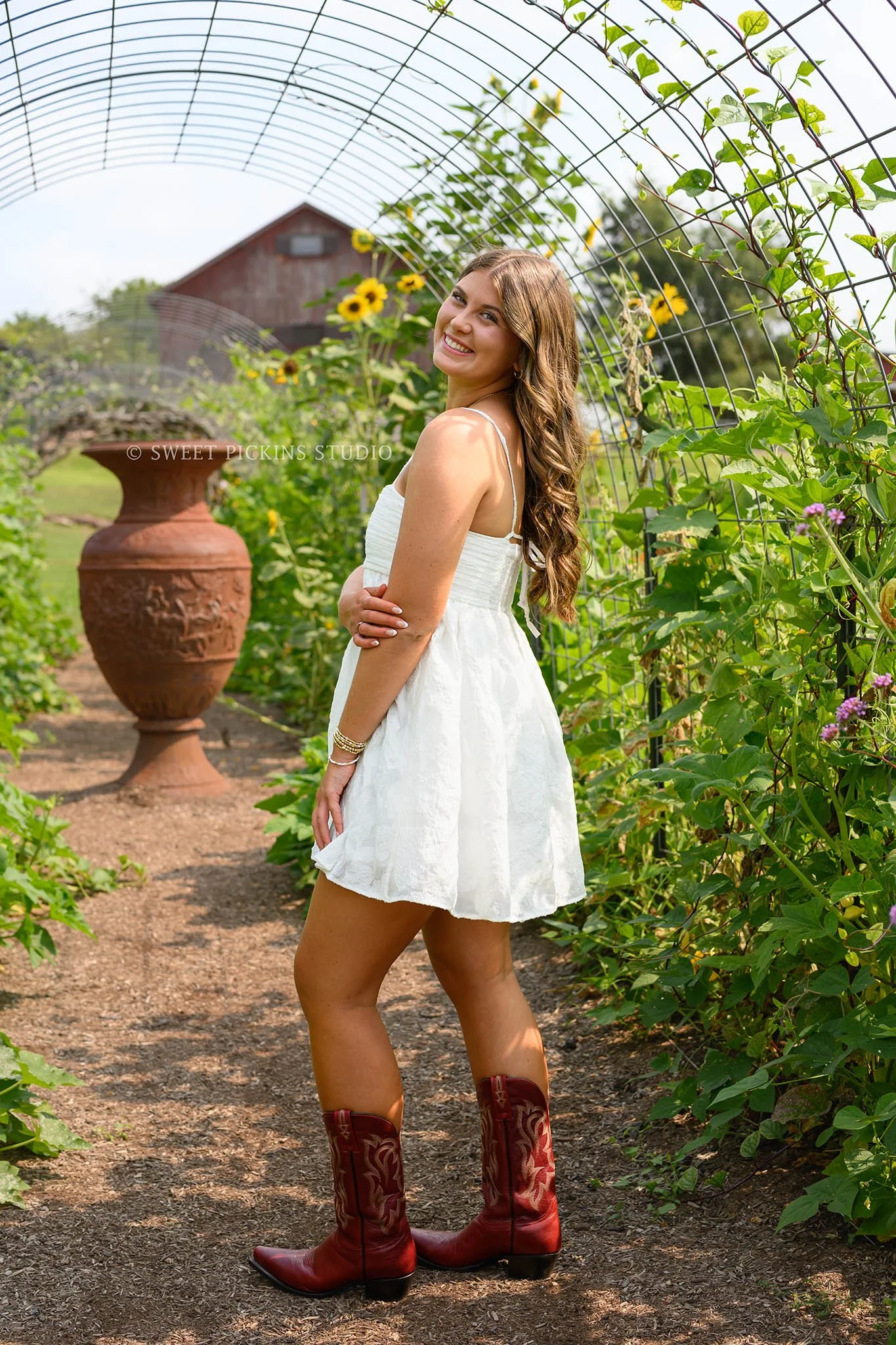 Zionsville, Indiana Country Senior Portrait Photography at Traders Point Creamery with class of 2027 senior girl posing in white dress and red western boots in country garden by Sweet Pickins Studio senior photographer Amanda Wilson ©