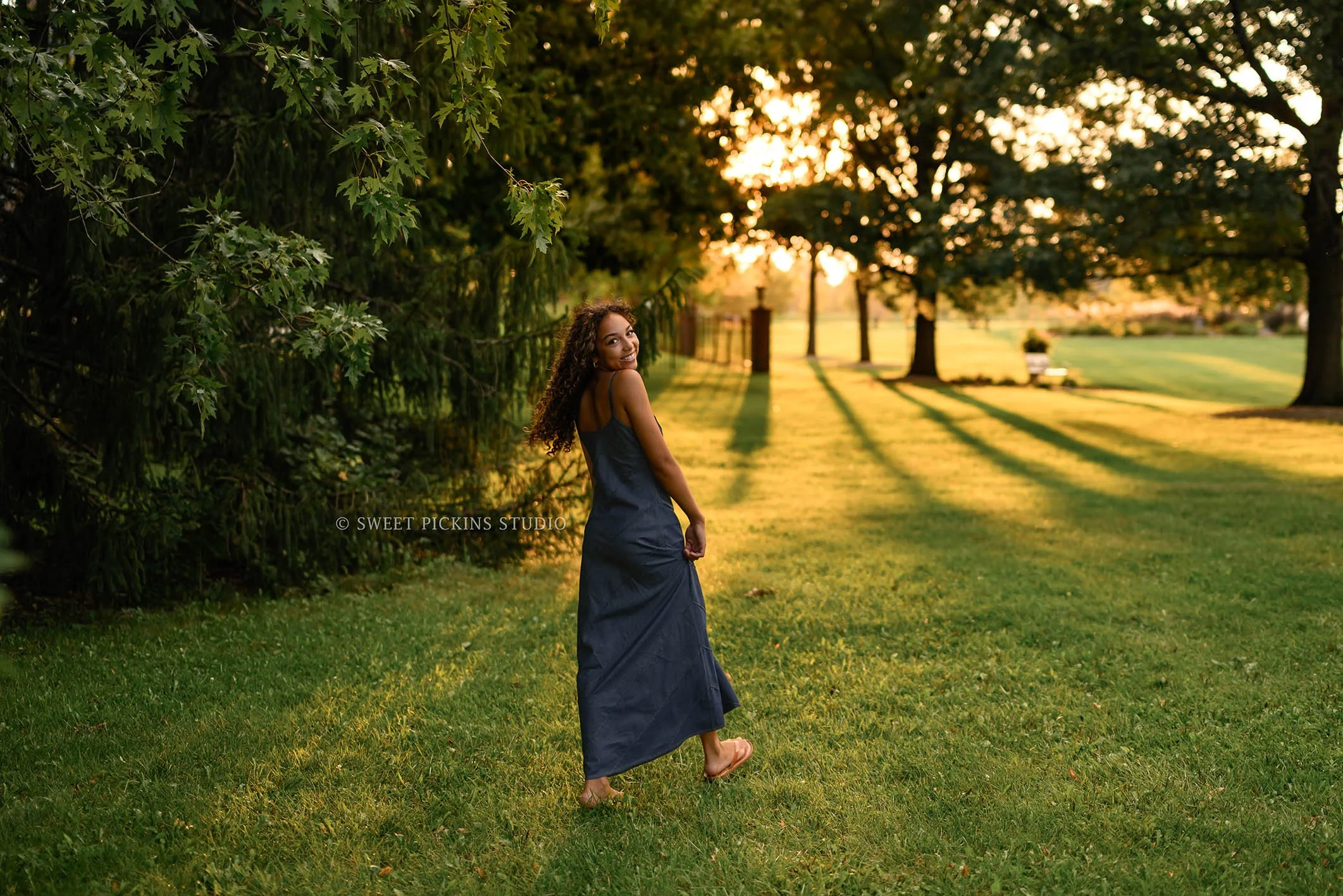 Madeline | Golden Hour Senior Photography for Class of 2027 senior girl with curly hair wearing denim jean dress walking in sunshine by Peru Indiana Senior  photographer Amanda Wilson of Sweet Pickins Studio ©