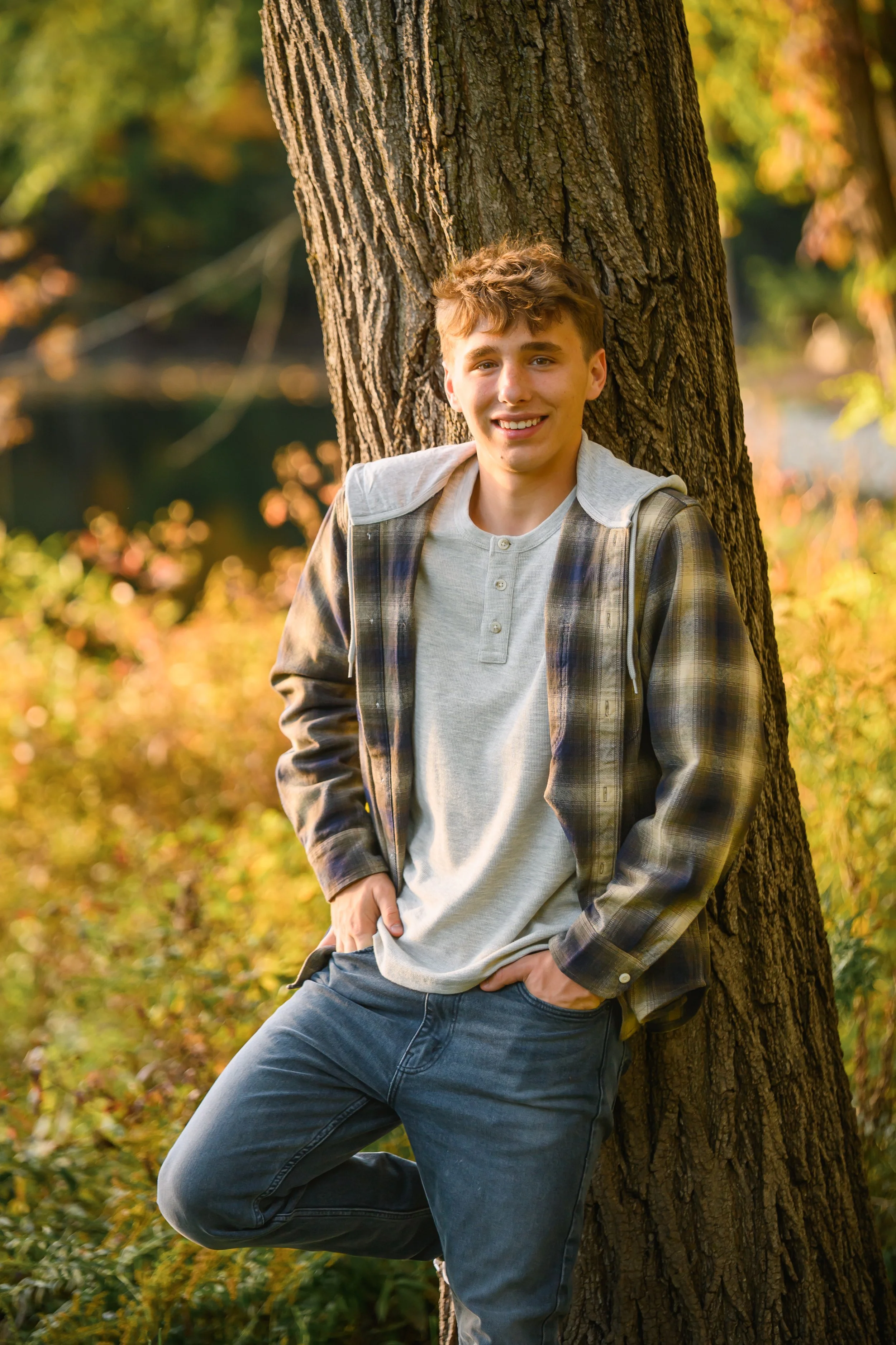 Huntington, Indiana Fall Senior Photography for Huntington North Class of 2027 senior guy BOSTAN leaning on tree at outdoor nature park wearing plaid flannel by Sweet Pickins Studio senior photographer Amanda Wilson ©