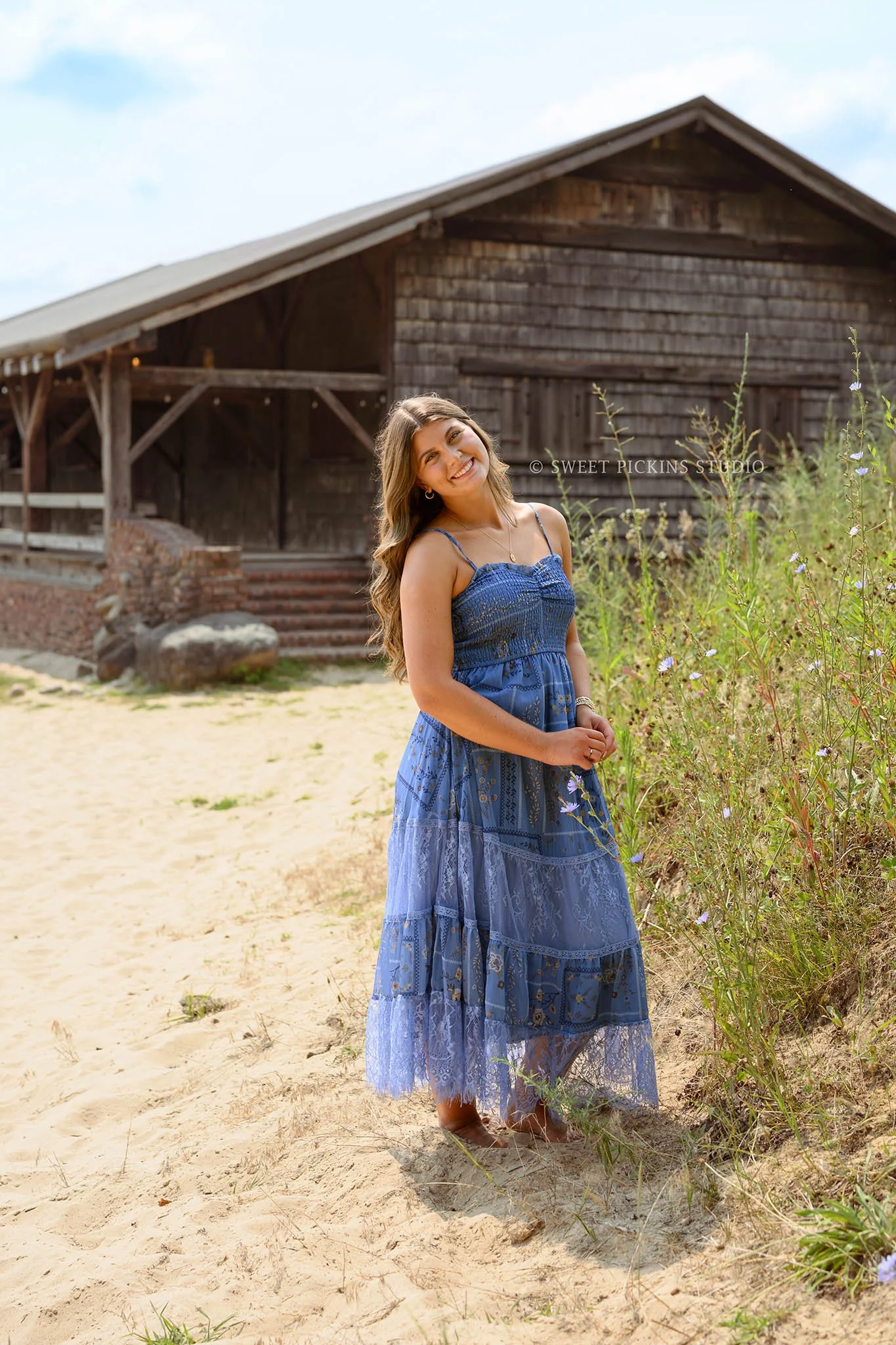 Zionsville, Indiana Senior Photography at Traders Point Creamery with class of 2027 senior girl posing in blue sun dress in beach sand by barn by Sweet Pickins Studio senior photographer Amanda Wilson ©