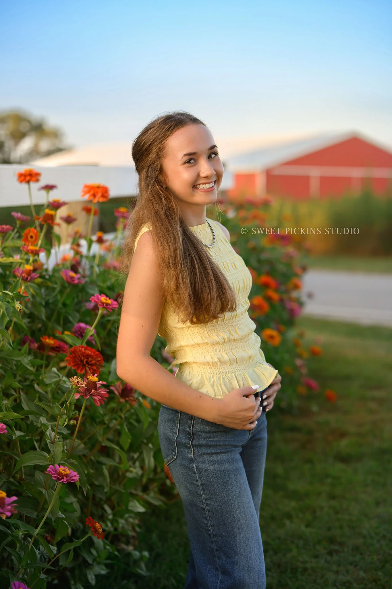 Natalie’s Lowell, Indiana Floral Senior Photography for class of 2027 senior girl posing with colorful zinnia flowers by red barn at  family farm by Sweet Pickins Studio senior photographer Amanda Wilson ©