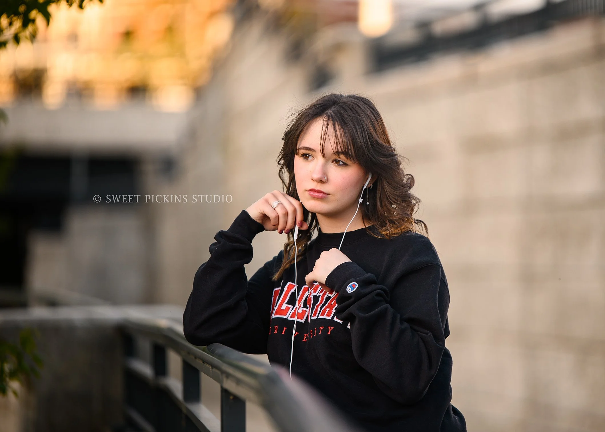 Hailee | Noblesville High School Graduation Photography in Cap and Gown in Downtown wearing college sweatshirt and earbuds listening to music by Sweet Pickins Studio senior photographer Amanda Wilson ©