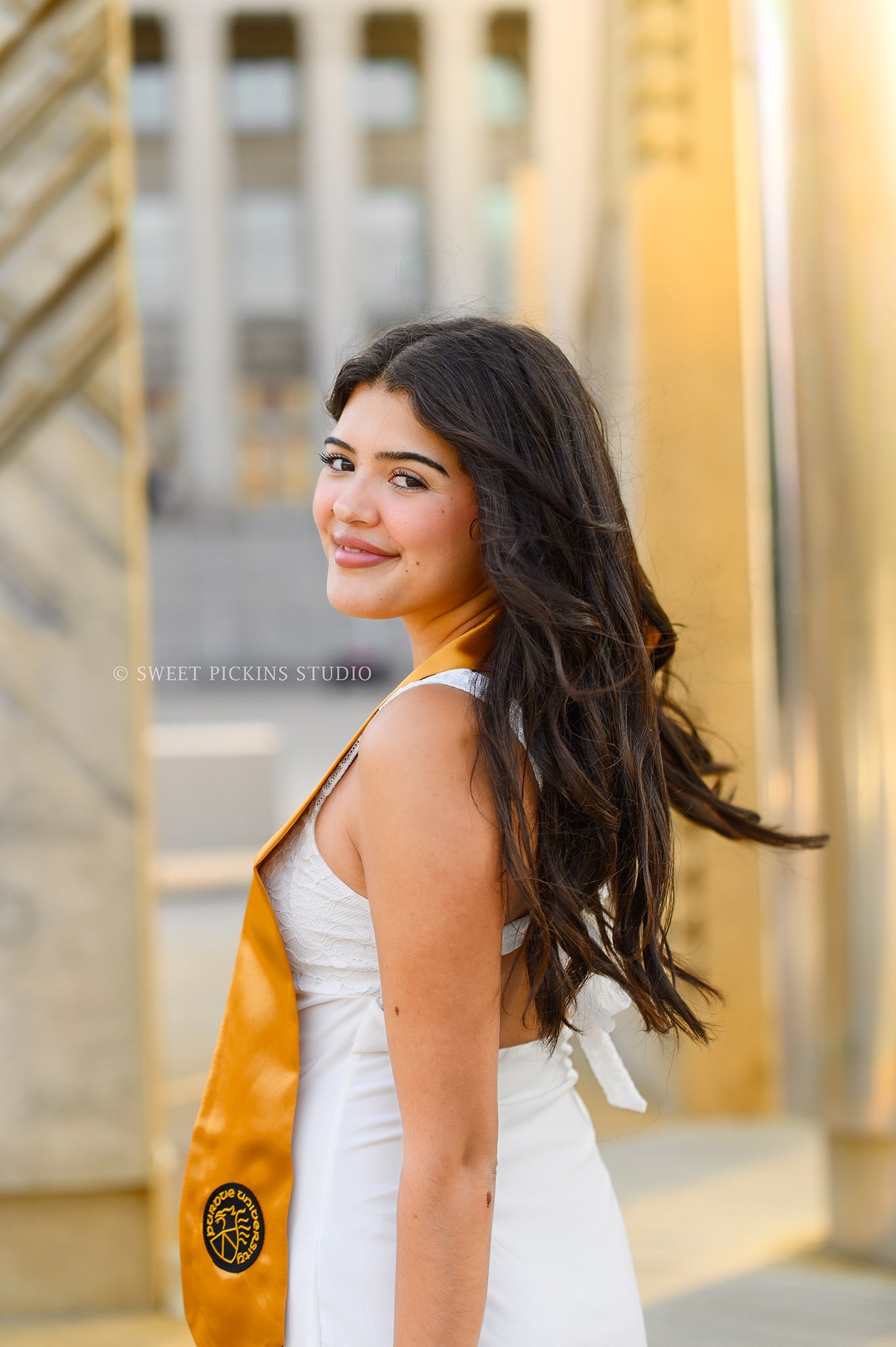 Maria’s Purdue University Graduation Portraits in West Lafayette, Indiana by Sweet Pickins Studio photographer Amanda Wilson for spring graduate posing in white dress at Engineering Fountain with grad cap and tassel © 2026