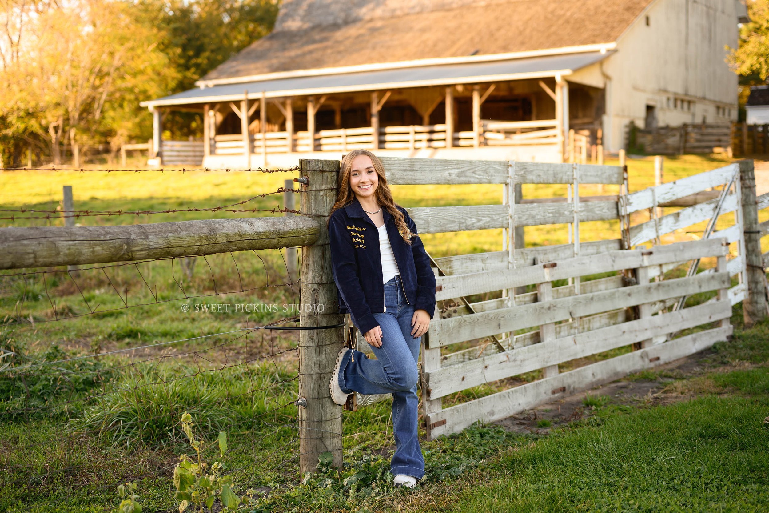 Indiana FFA Senior Pictures for class of 2027 senior girl wearing official blue jacket posing by farm fence near barn by Sweet Pickins Studio senior photographer Amanda Wilson ©