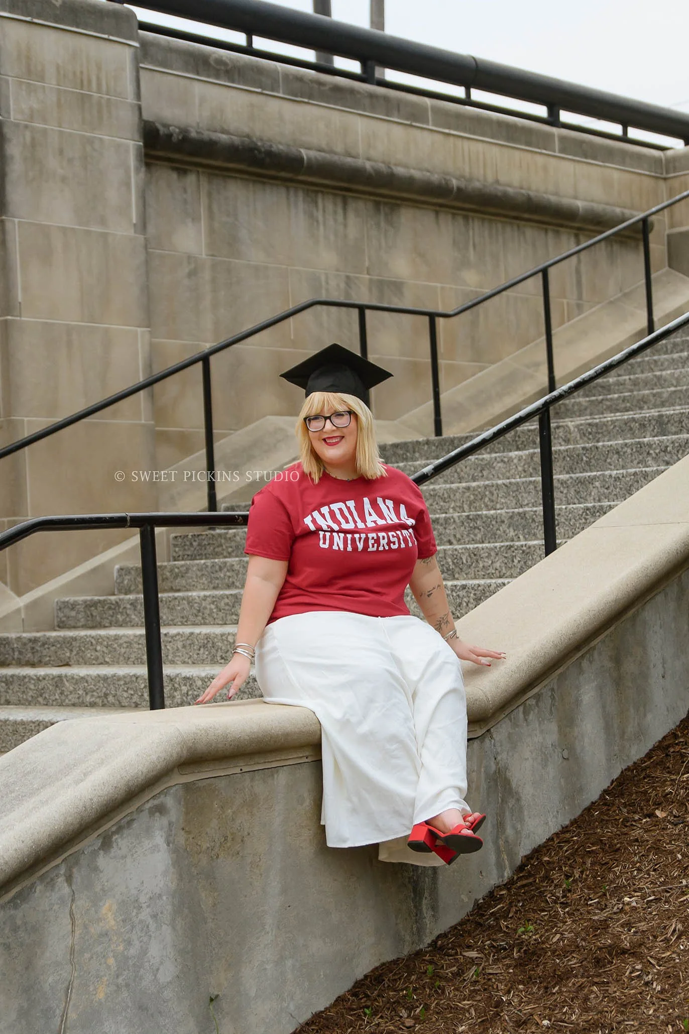 I.U. Indy Graduation Photography in Downtown Indianapolis, Indiana for class of 2026 spring grad wearing red school t-shirt and white skirt by canal by Sweet Pickins Studio senior photographer Amanda Wilson ©
