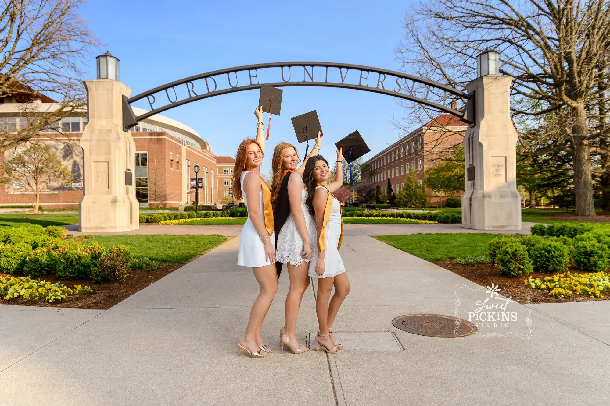 Purdue Graduation Photography for Sorority Sisters in West Lafayette, Indiana by Sweet Pickins Studio photographer Amanda Wilson for graduates posing in white dresses at Engineering arch with grad caps with tassels © 2026