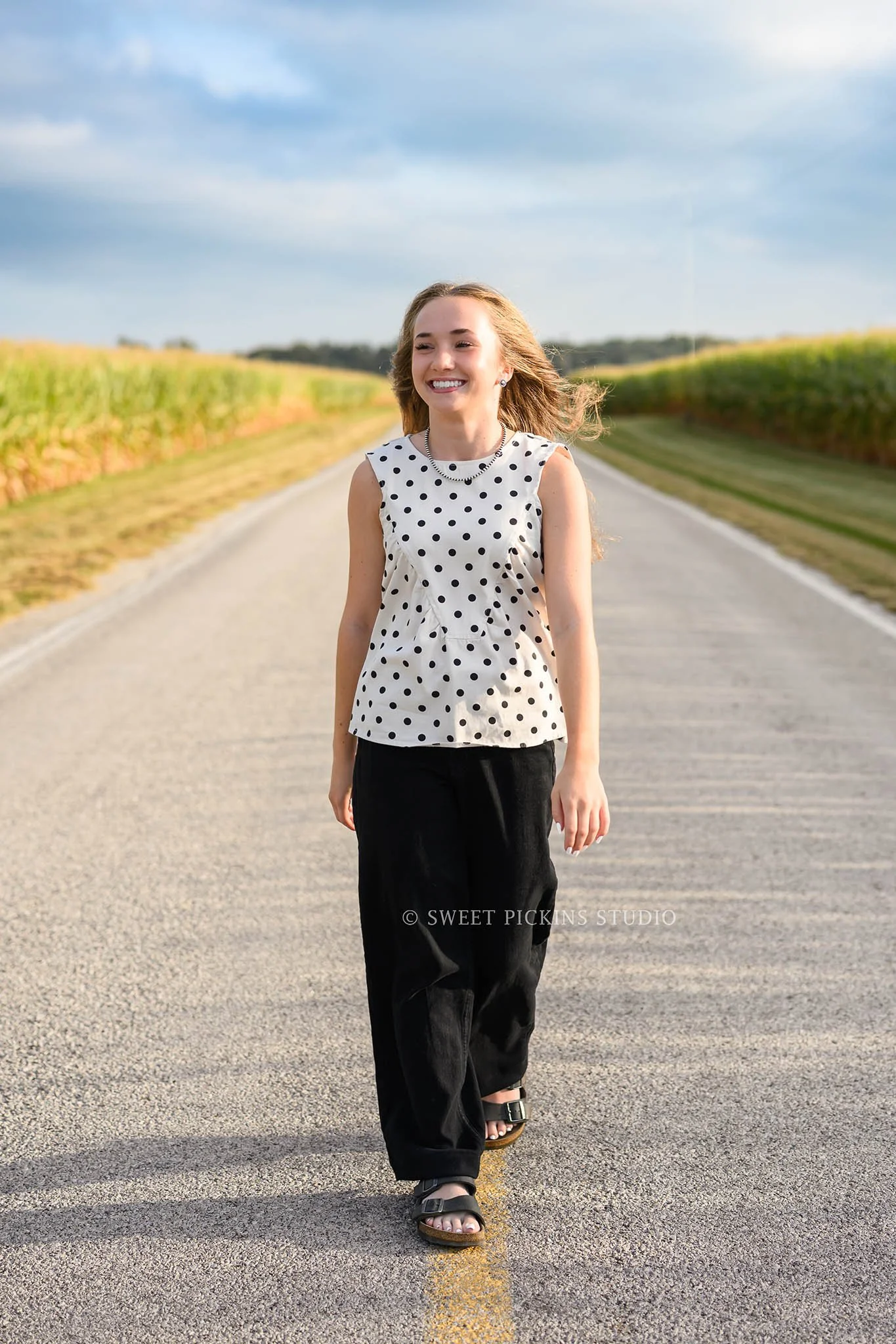 Natalie’s Lowell, Indiana Senior Girl Photography for class of 2027 posing in the middle of country road wearing black polka dot top by Sweet Pickins Studio senior photographer Amanda Wilson ©