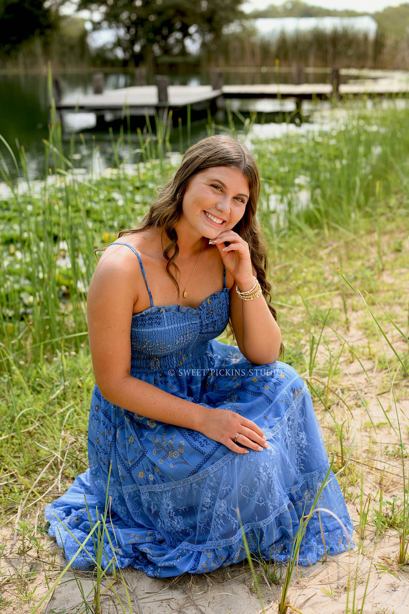 Zionsville, Indiana Senior Photography at Traders Point Creamery with class of 2027 senior girl posing in blue sun dress in beach sand by wood pier at lake by Sweet Pickins Studio senior photographer Amanda Wilson ©