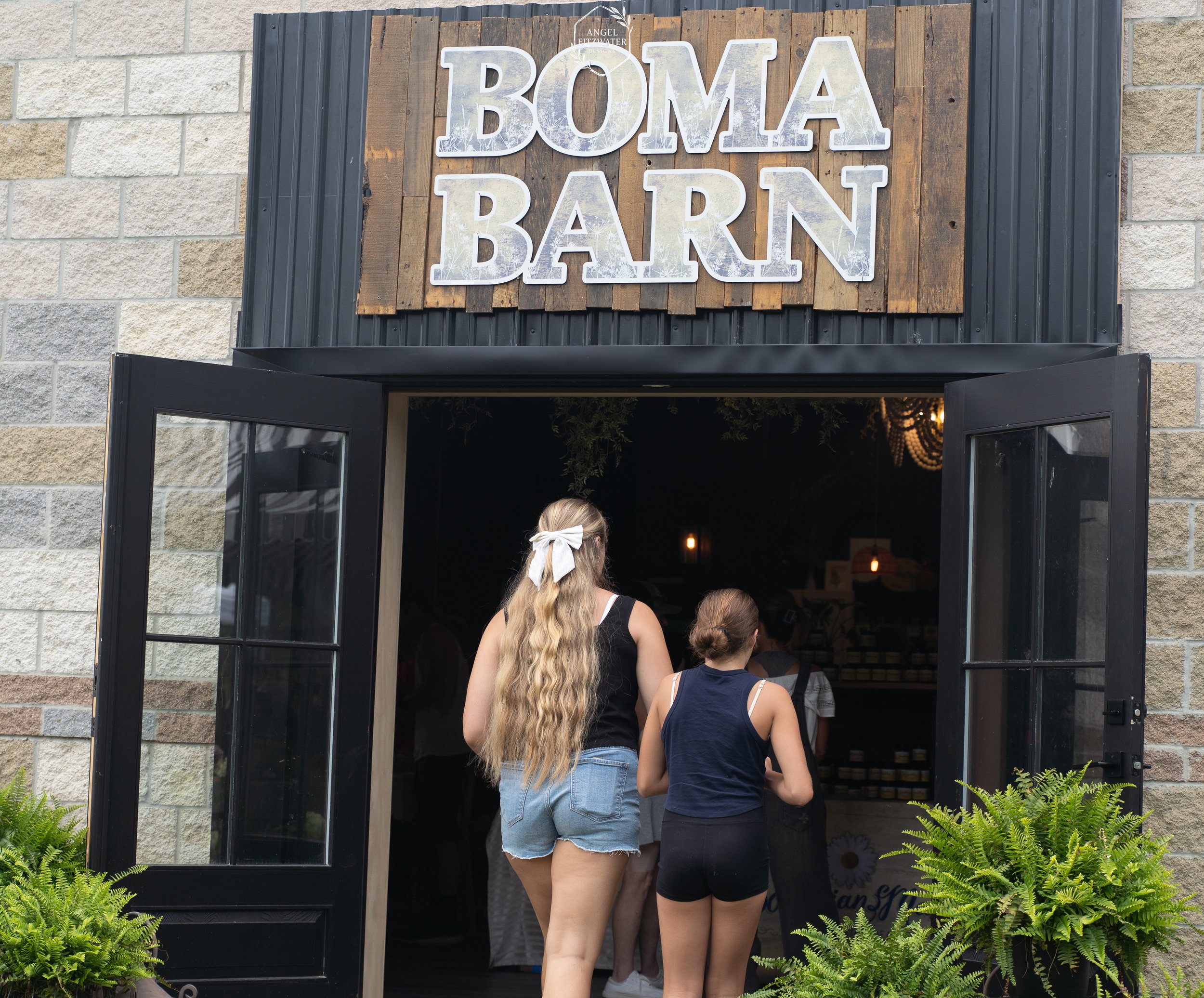 People walking into Boma Barn through open black-framed doors beneath a wooden sign. The sign reads 'BOMA BARN' in large white letters.