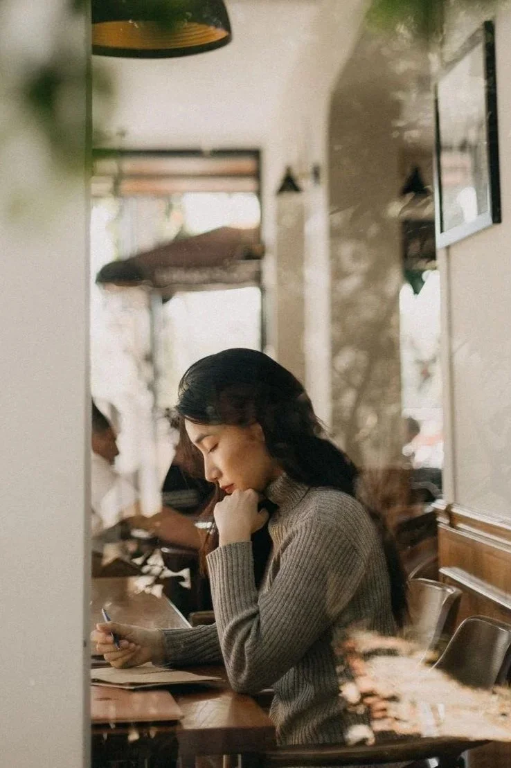 Woman writing in a notebook at a café, an example of challenging a cognitive distortion through reframing, Hoboken NJ therapist