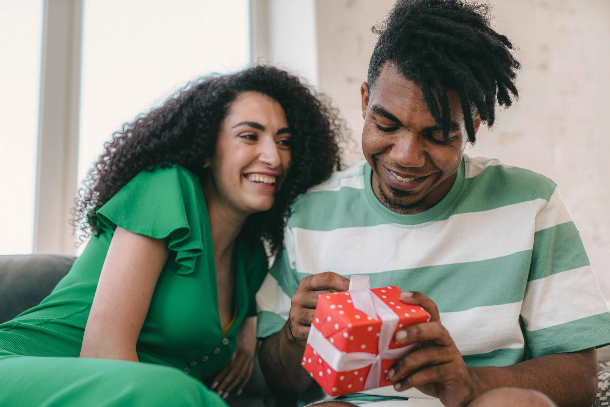 Man opening a wrapped gift from his girlfriend on the couch, love bombing signs Hoboken NJ therapist