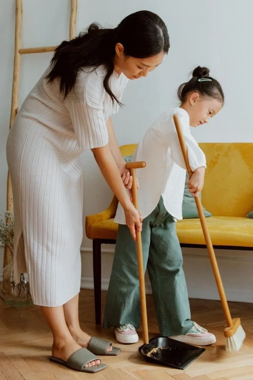Mother helping her young daughter sweep the living room floor, family roles psychology Hoboken NJ counselor