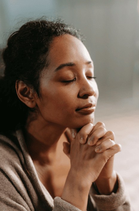 a woman with eyes closed and hands together praying in NJ due to religious trauma