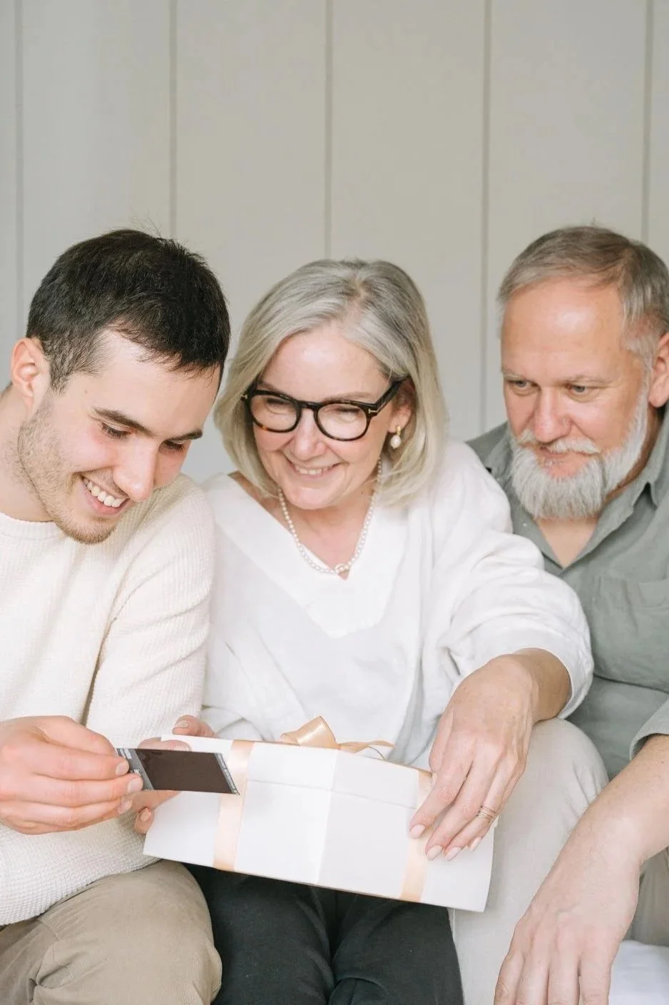 Young man opening a gift box with his smiling parents beside him on a couch, how to deal with a narcissistic parent Hoboken NJ therapist