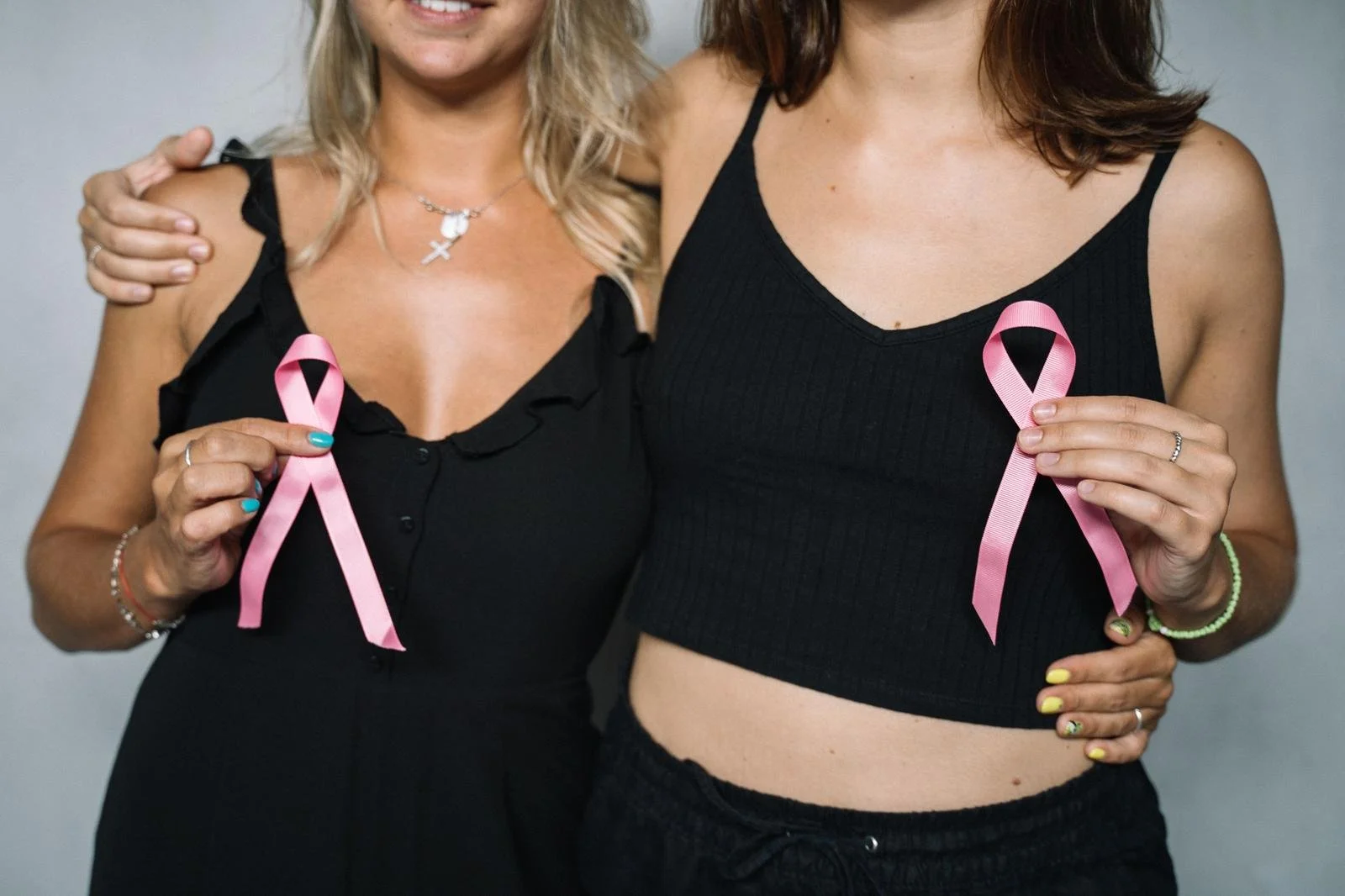 Two women smiling and holding pink ribbons together, an example of post traumatic growth after illness, Hoboken NJ therapist