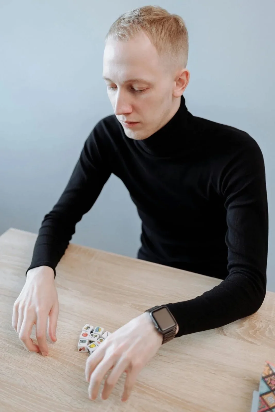 A man in a black turtleneck sits alone at a table carefully arranging small objects, symbolizing the repetitive and compulsive behaviors associated with OCD obsessive thought patterns