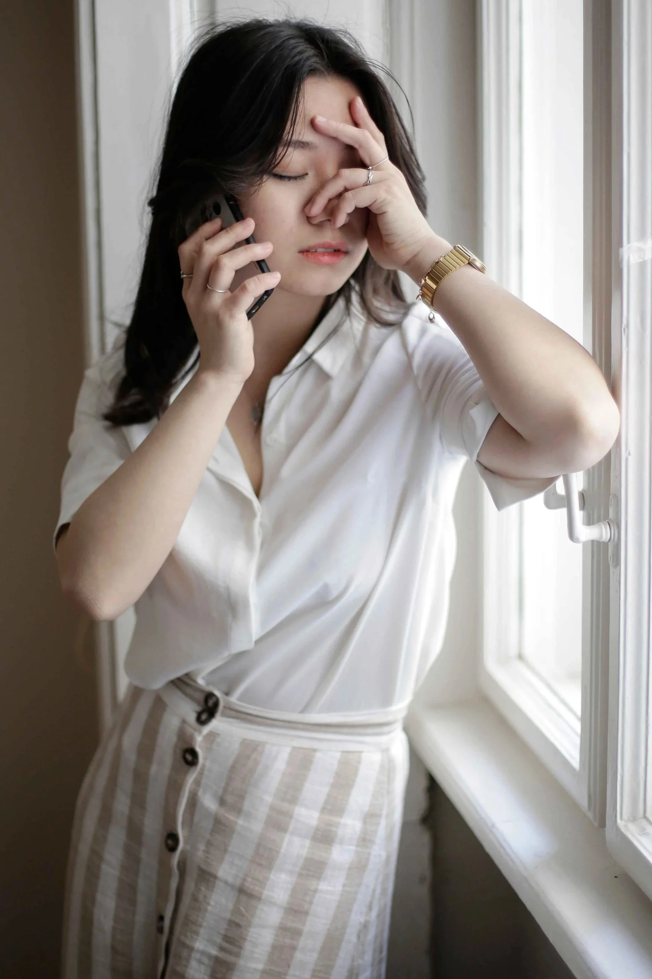 A young woman experiencing phone call anxiety holds her phone and rubs her face during a stressful call, a common concern treated by therapists at Anchor Therapy in Hoboken, NJ.