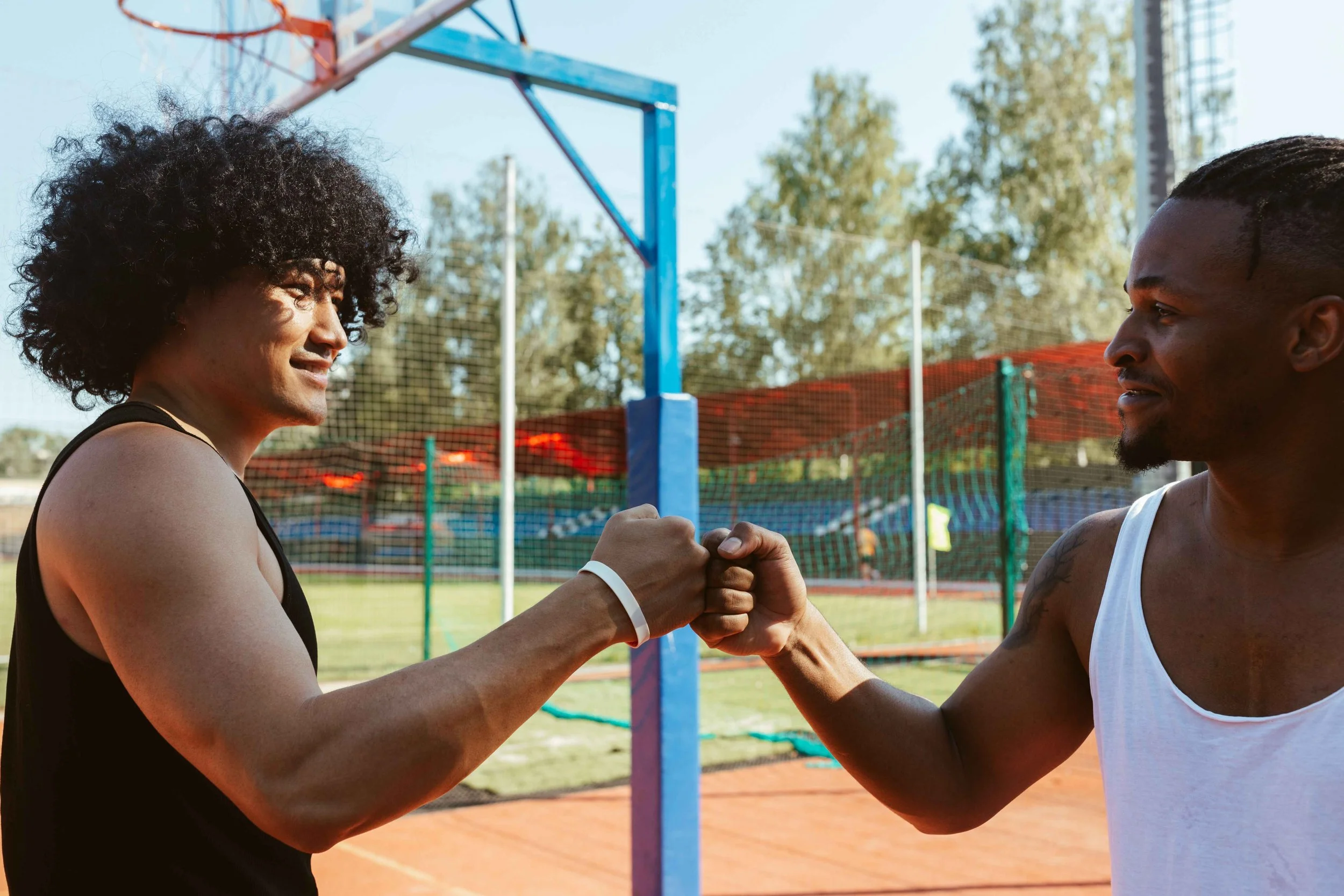 Two men fist-bumping and smiling on a basketball court, an example of healthy competition between friends, Hoboken NJ therapist