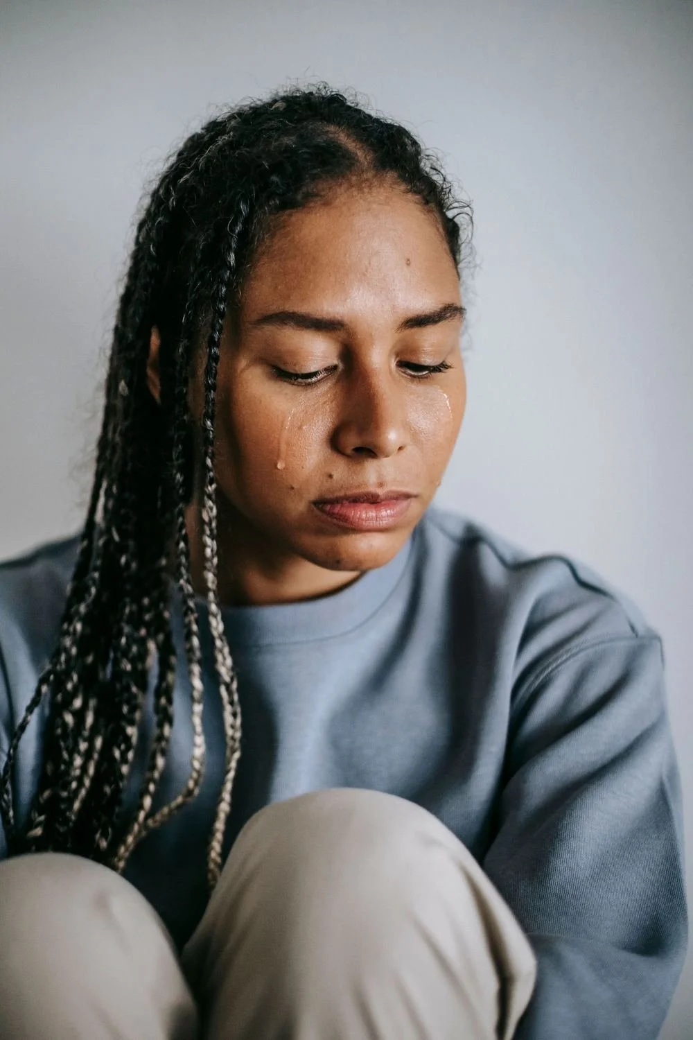 Woman with tears on her cheeks sitting with her knees pulled up and looking down, grief and loneliness Hoboken NJ therapist