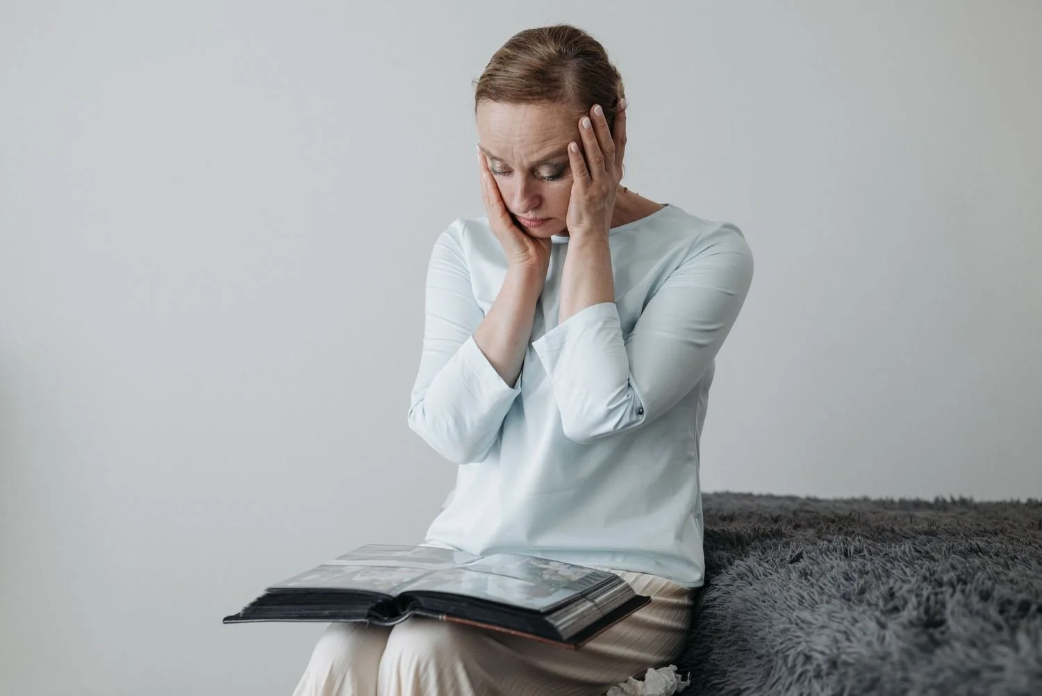 Woman sitting on the edge of a bed holding her face while looking through a photo album, OCD false memories Hoboken NJ therapist