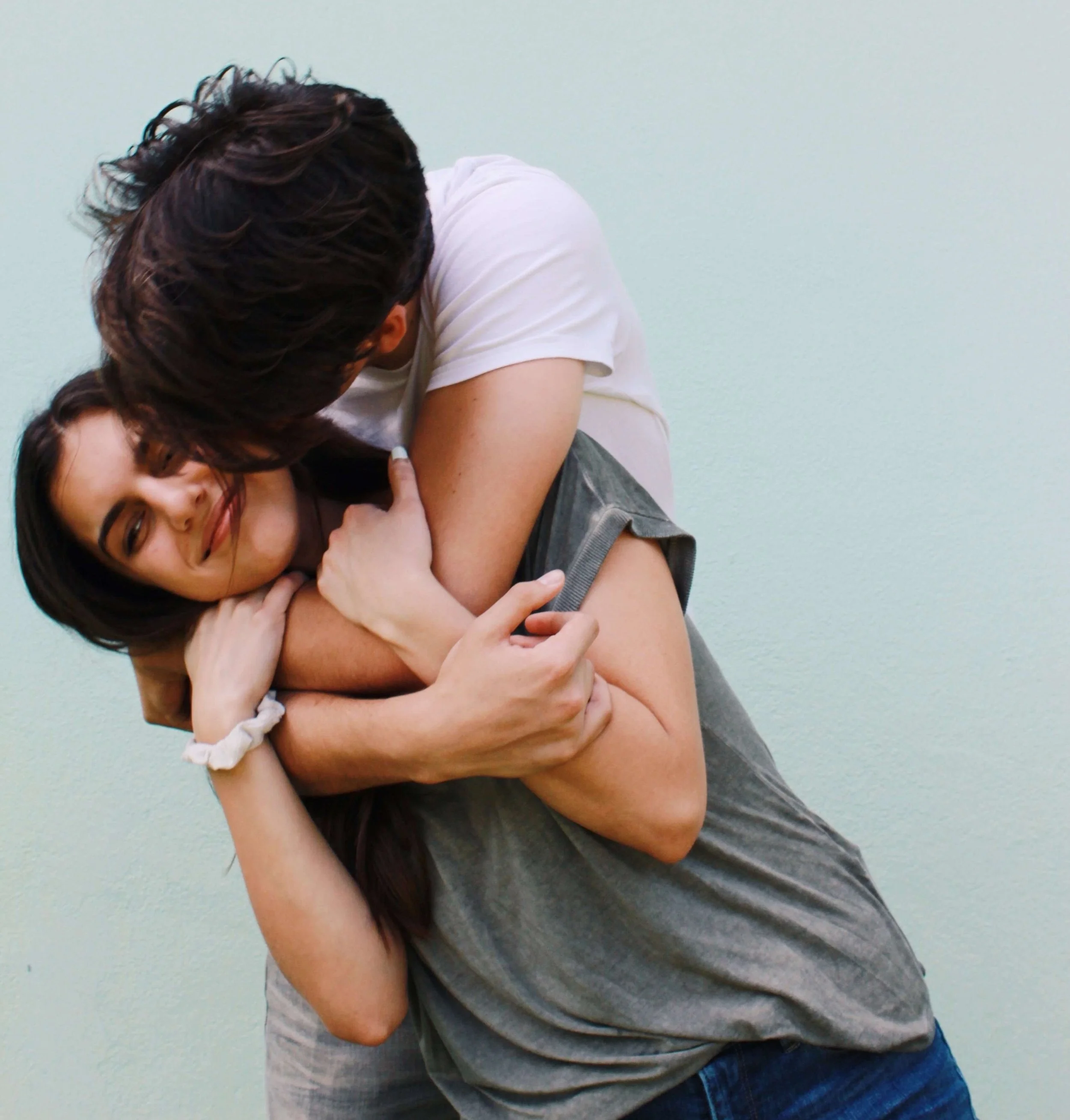 Couple sharing a playful, close embrace, one partner's face turned away from the camera, situationship in Hoboken, NJ