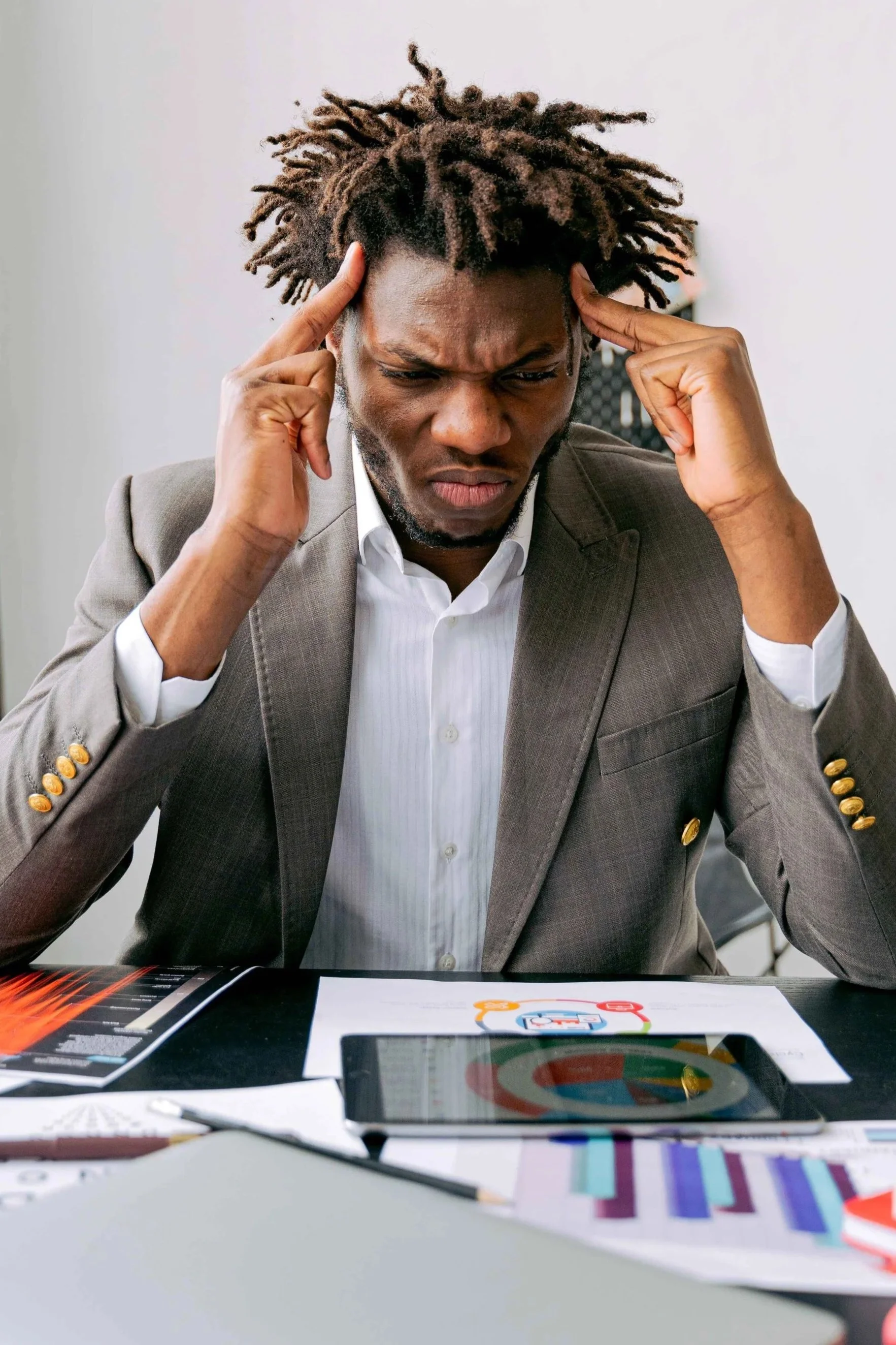 Man pressing his fingers to his temples while looking at charts and data, an example of anxiety during decision-making, Hoboken NJ therapist