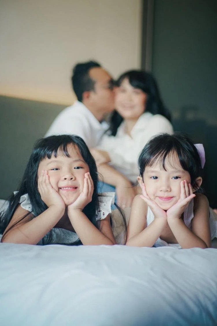 Two young sisters smiling with their parents embracing behind them, an example of positive emotional contagion in a family, Hoboken NJ therapist