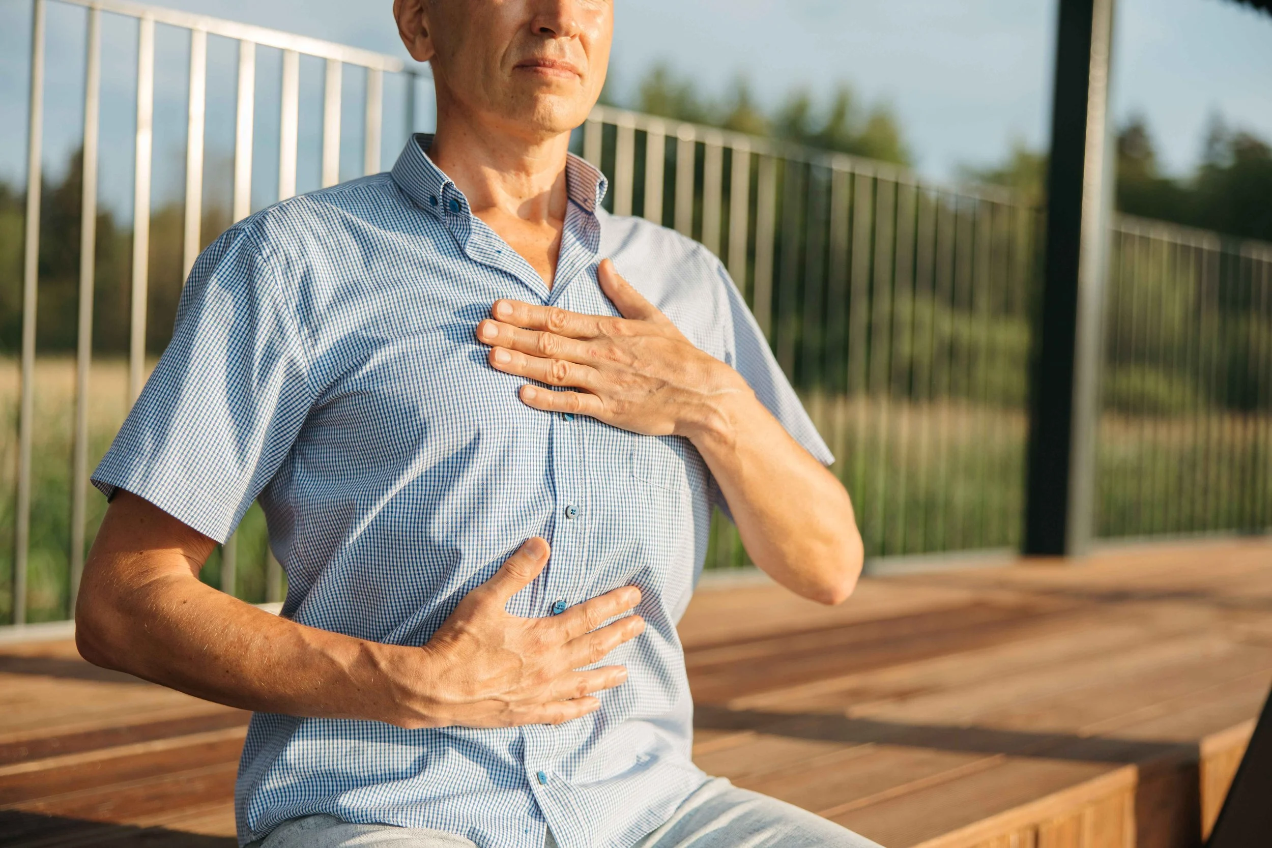 Man sitting outdoors with one hand on his chest and one on his stomach, an example of monitoring breathing in somatic OCD, Hoboken NJ therapist