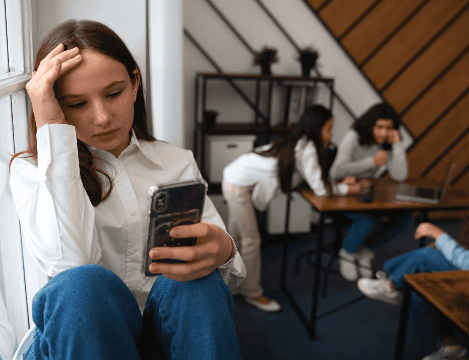 a young girl on her phone sitting by the window away from others due to social anxiety in Jersey City NJ