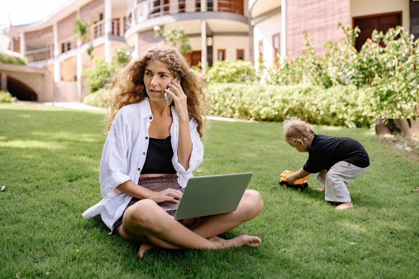 Woman on a work call with her laptop open while her child plays nearby, an example of blurred work-life boundaries, Hoboken NJ therapist