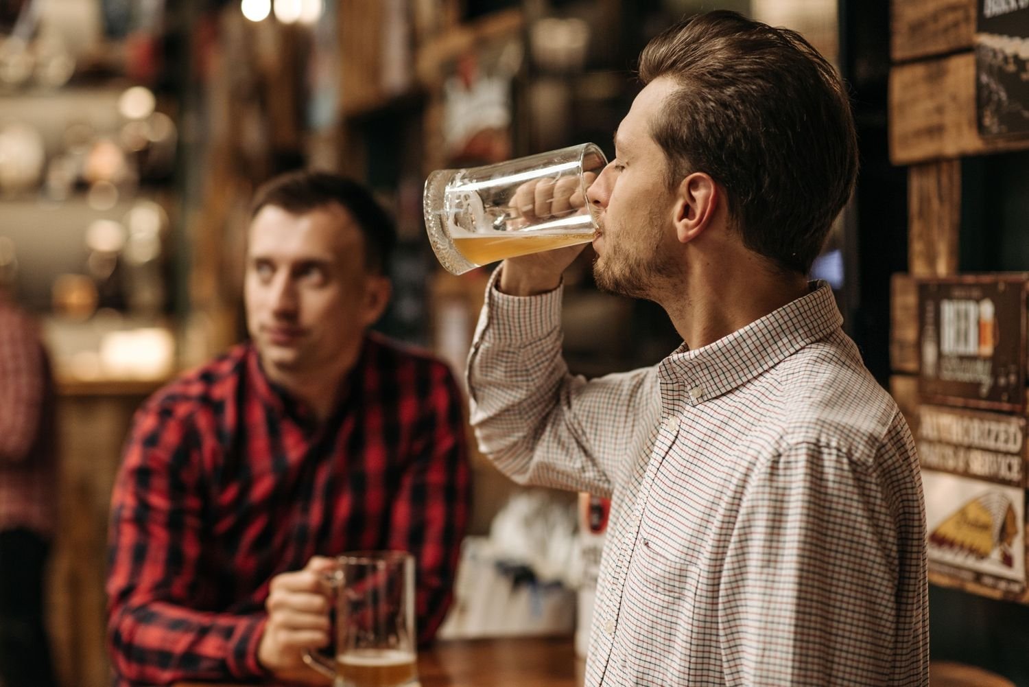 Man drinking a large mug of beer at a bar as a friend looks on, high functioning alcoholic signs Hoboken NJ counselor