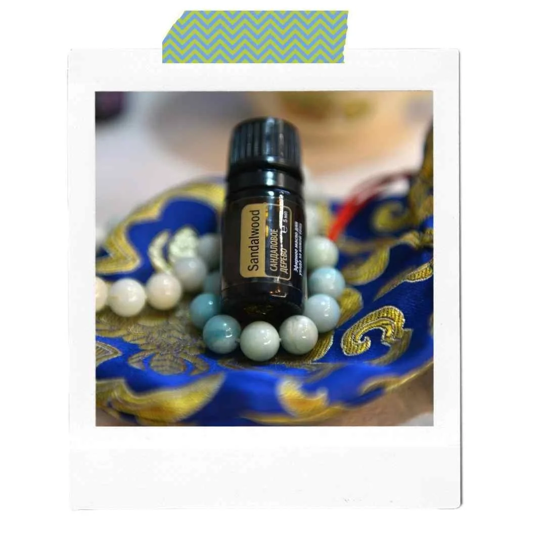 Ein Fläschchen mit Sandalwood-Ätheröl liegt auf einer Perlenkette, auf einem blauen, gold verzierten Stoff.