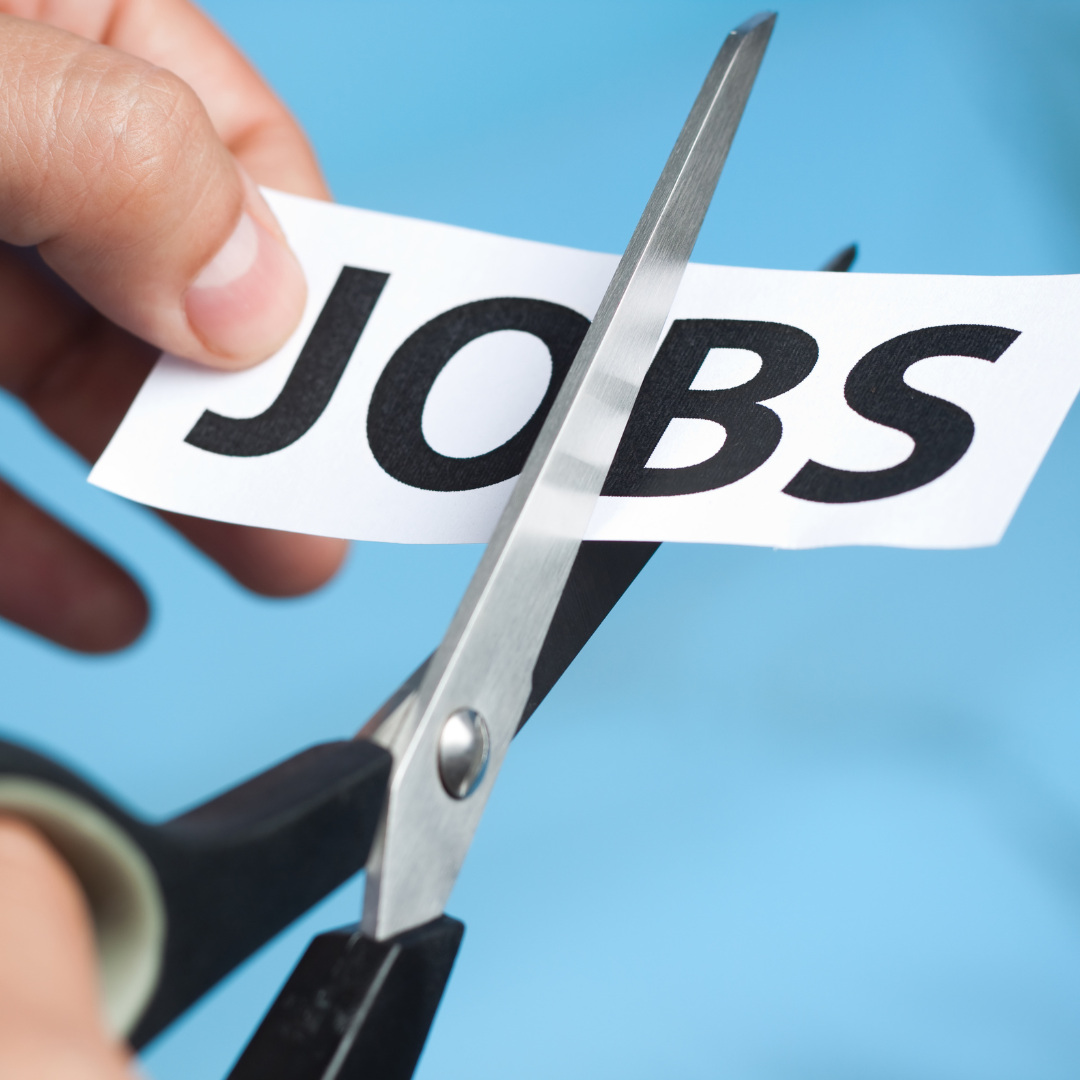 Close-up of scissors cutting a slip of paper with the word JOBS printed on it, representing corporate downsizing and Q2 2026 major company layoffs.