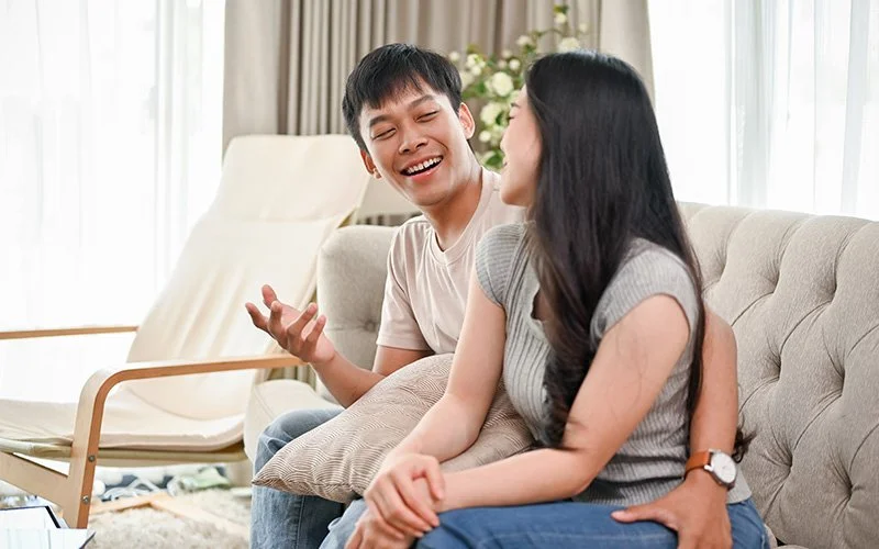 Singaporean couple laughing and talking on the sofa.