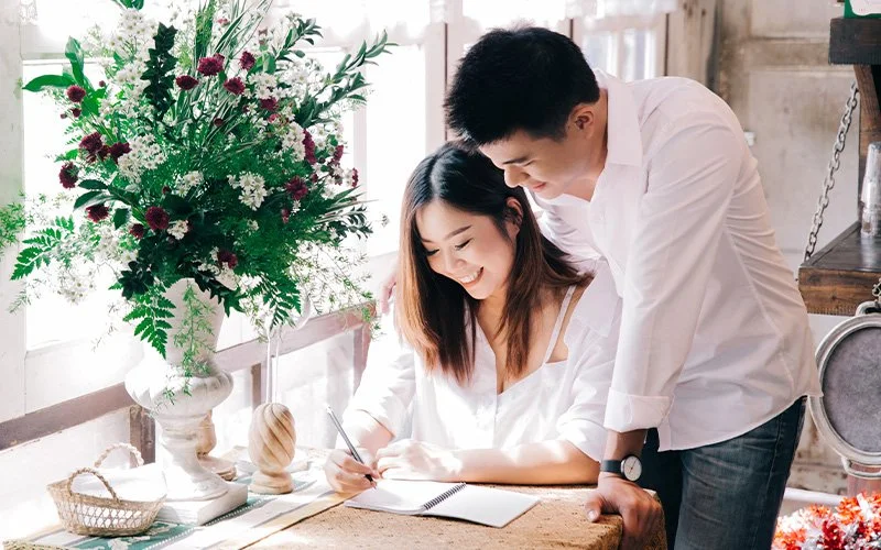 Smiling couple writing in a notebook together at home.