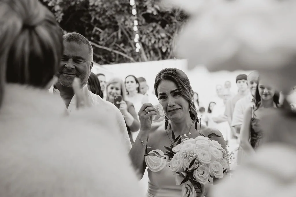 A emotional woman holding a bouquet of flowers at a wedding ceremony, surrounded by friends and family.