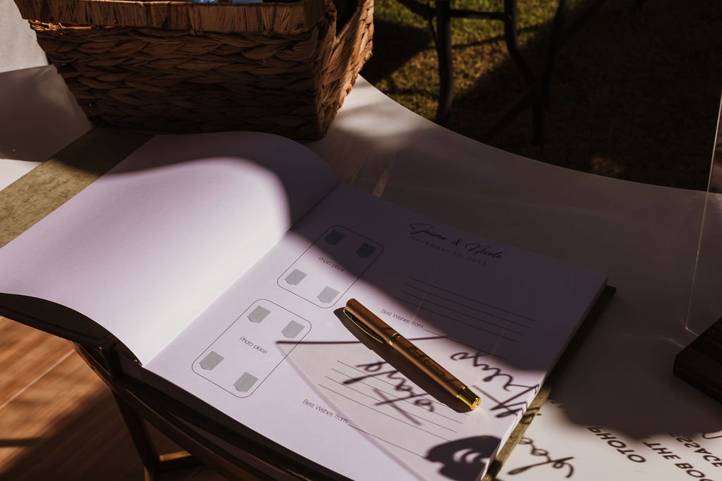 Open guest book on a table with a gold pen resting on it, in sunlight.