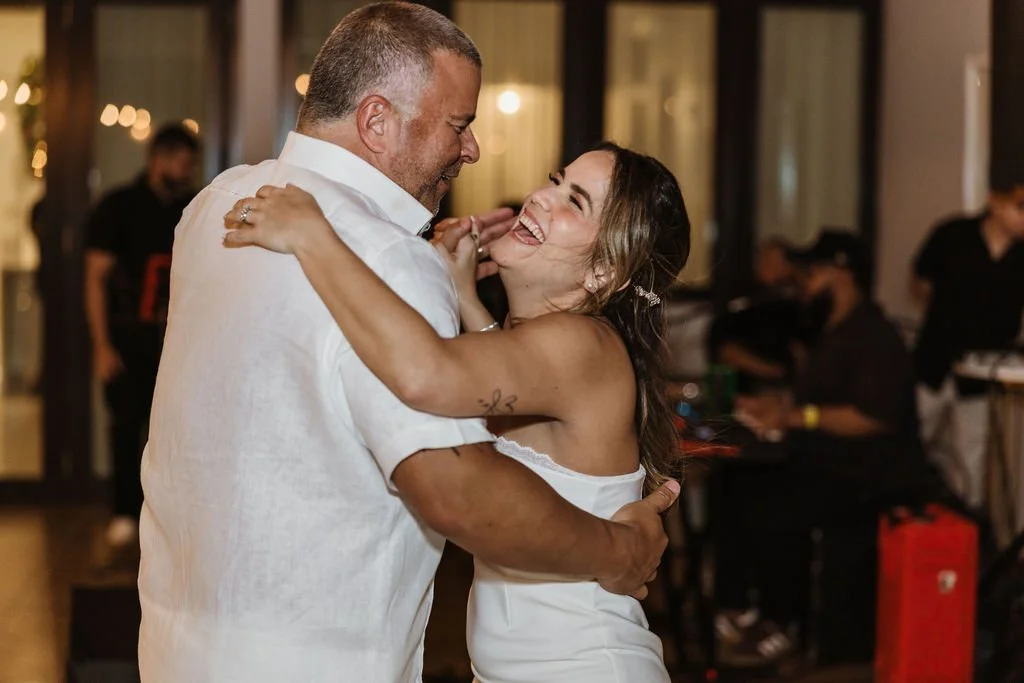 A couple dancing happily at an indoor event, with the woman smiling widely and the man embracing her.