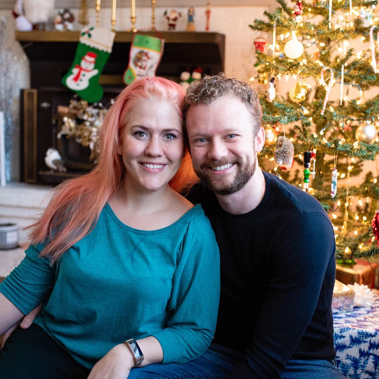 Leah Gunn Emerick and her husband sit smiling at the camera in front of their Christmas tree