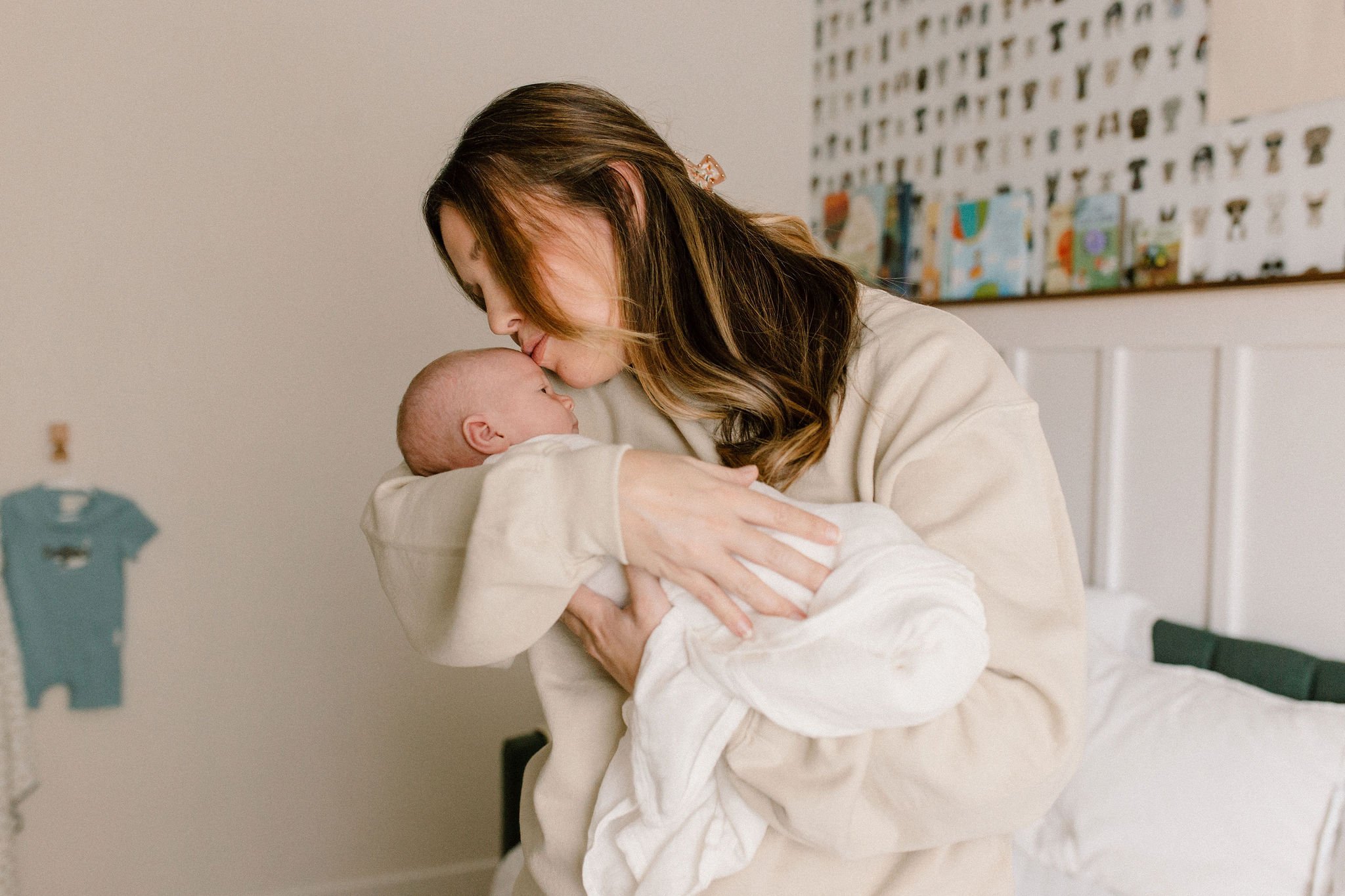 mom holding newborn baby kissing his forehead in neutral nursery