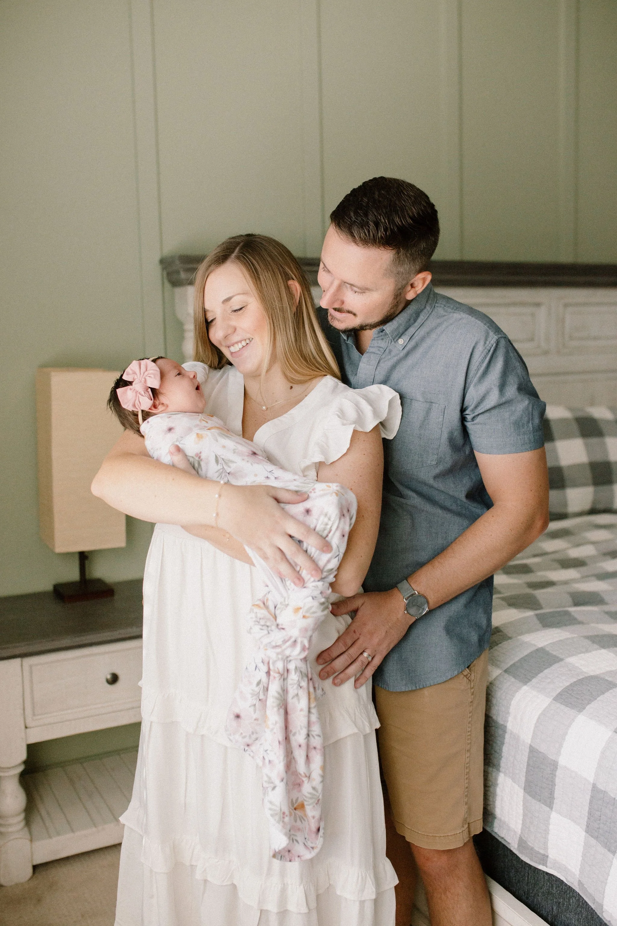 Mom and dad holding newborn baby in primary bedroom captured by Mesa newborn photographer