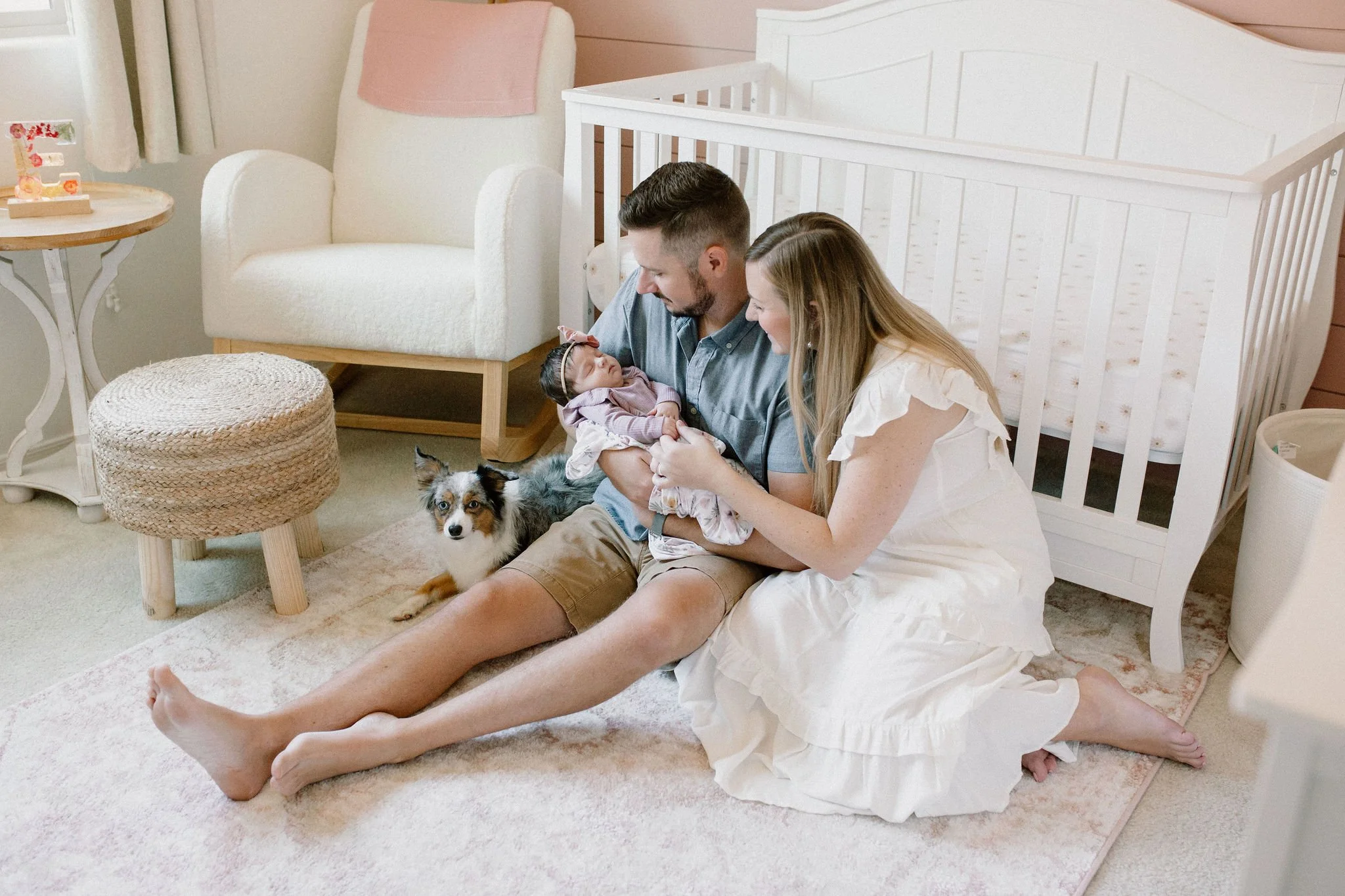 Mesa newborn photographer captures cuddly moment in nursery with mom and dad holding baby with dog nearby