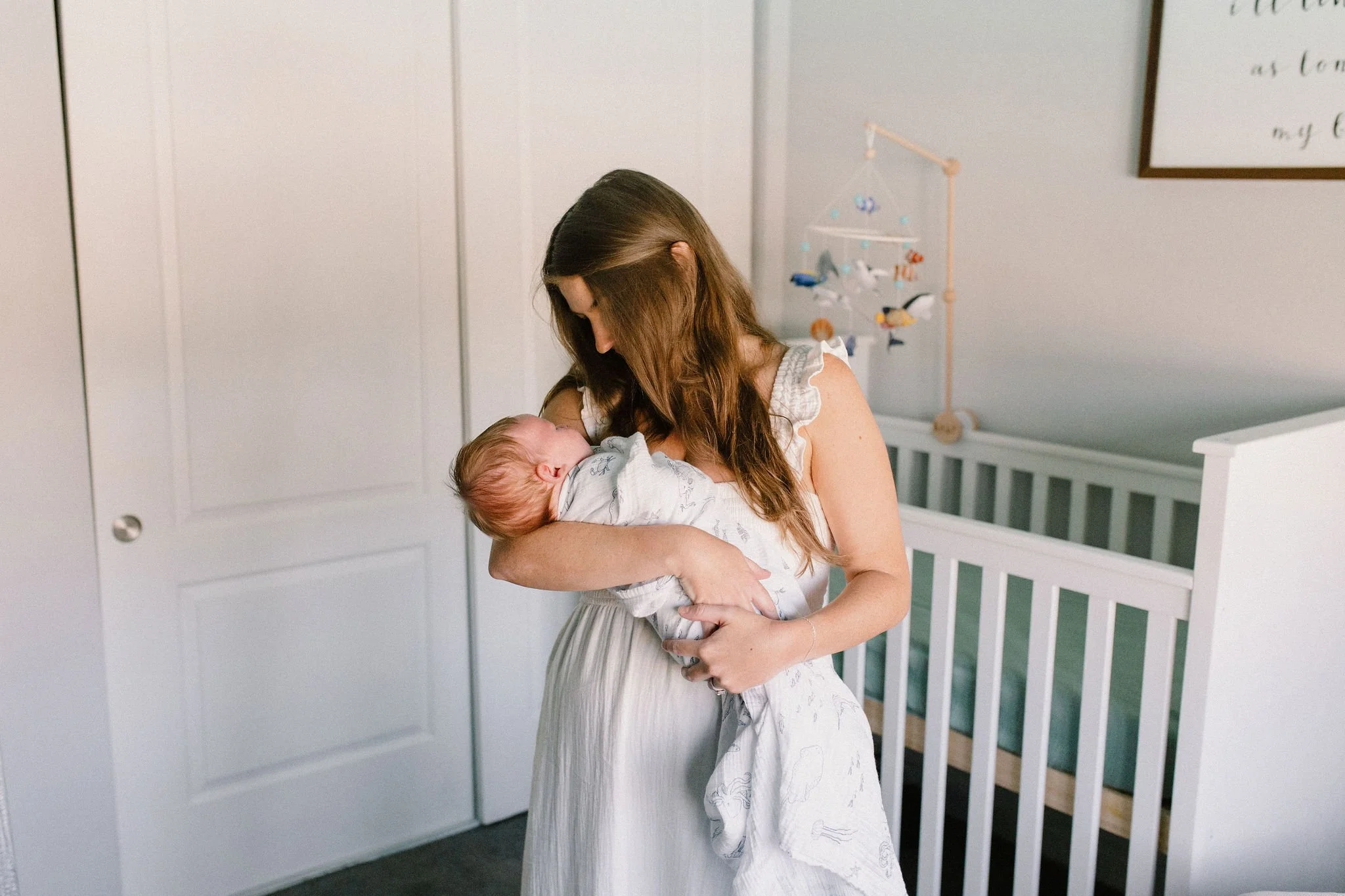 mom holding swaddled baby in nursery by Tempe Arizona newborn photographer