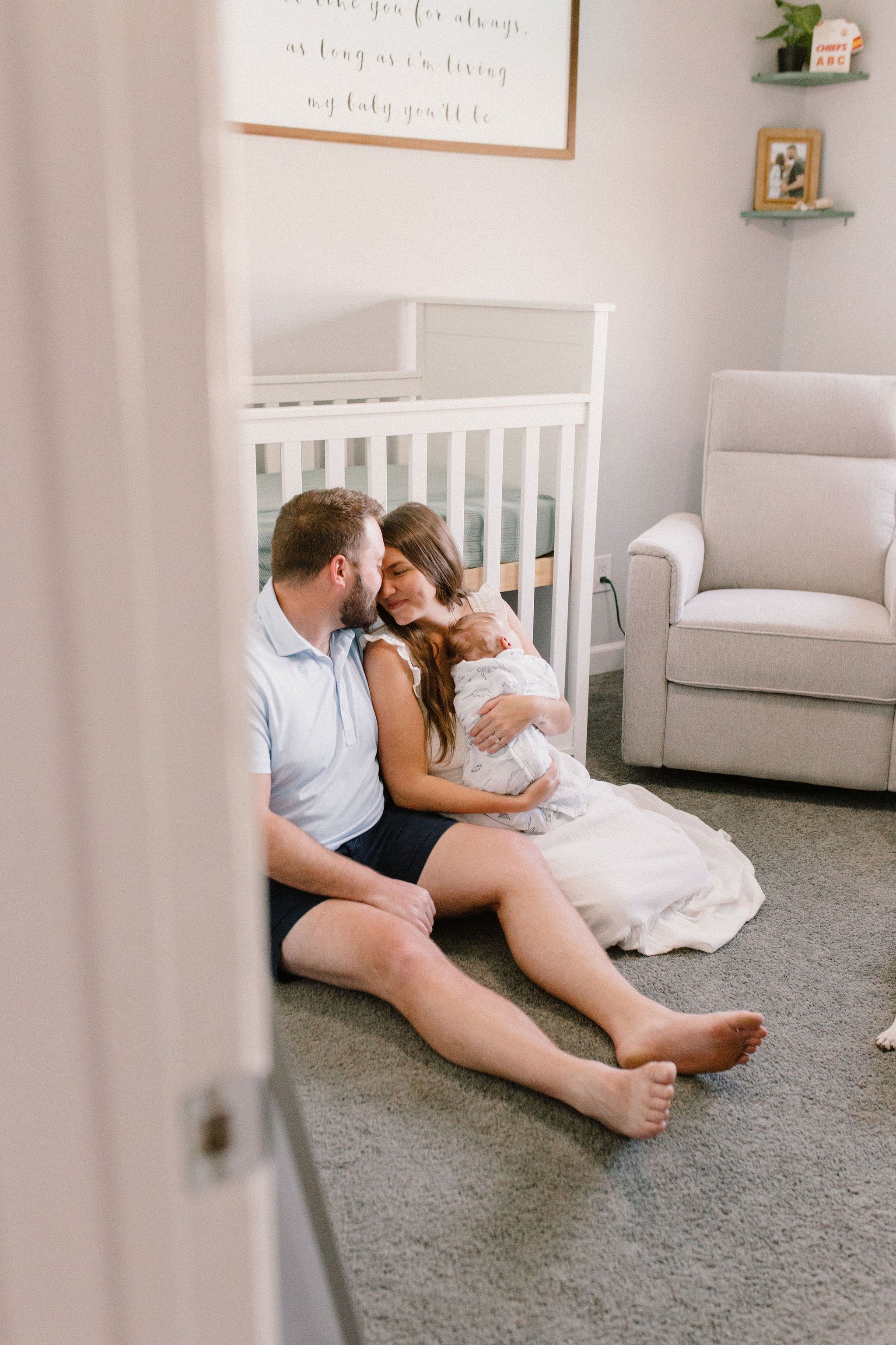 mom and dad holding baby in nursery sitting against crib captured by Tempe Arizona newborn photographer